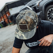 Hoonigan SPRINT unstructured snapback hat in camo, worn by a person in a casual setting, showcasing automotive lifestyle.