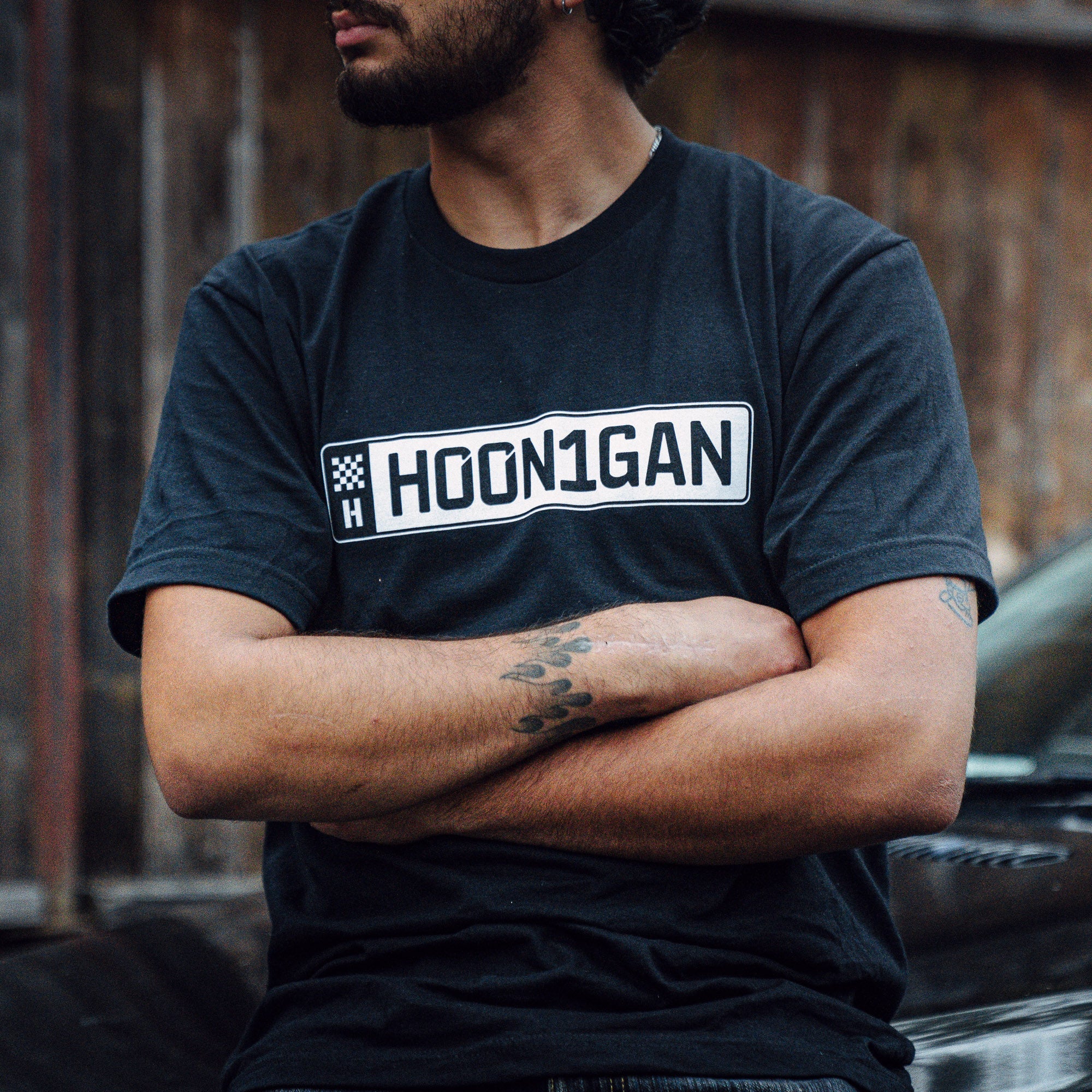 A person wearing a black Hoonigan AUTOBAHN short sleeve t-shirt, showcasing a bold logo, with arms crossed.