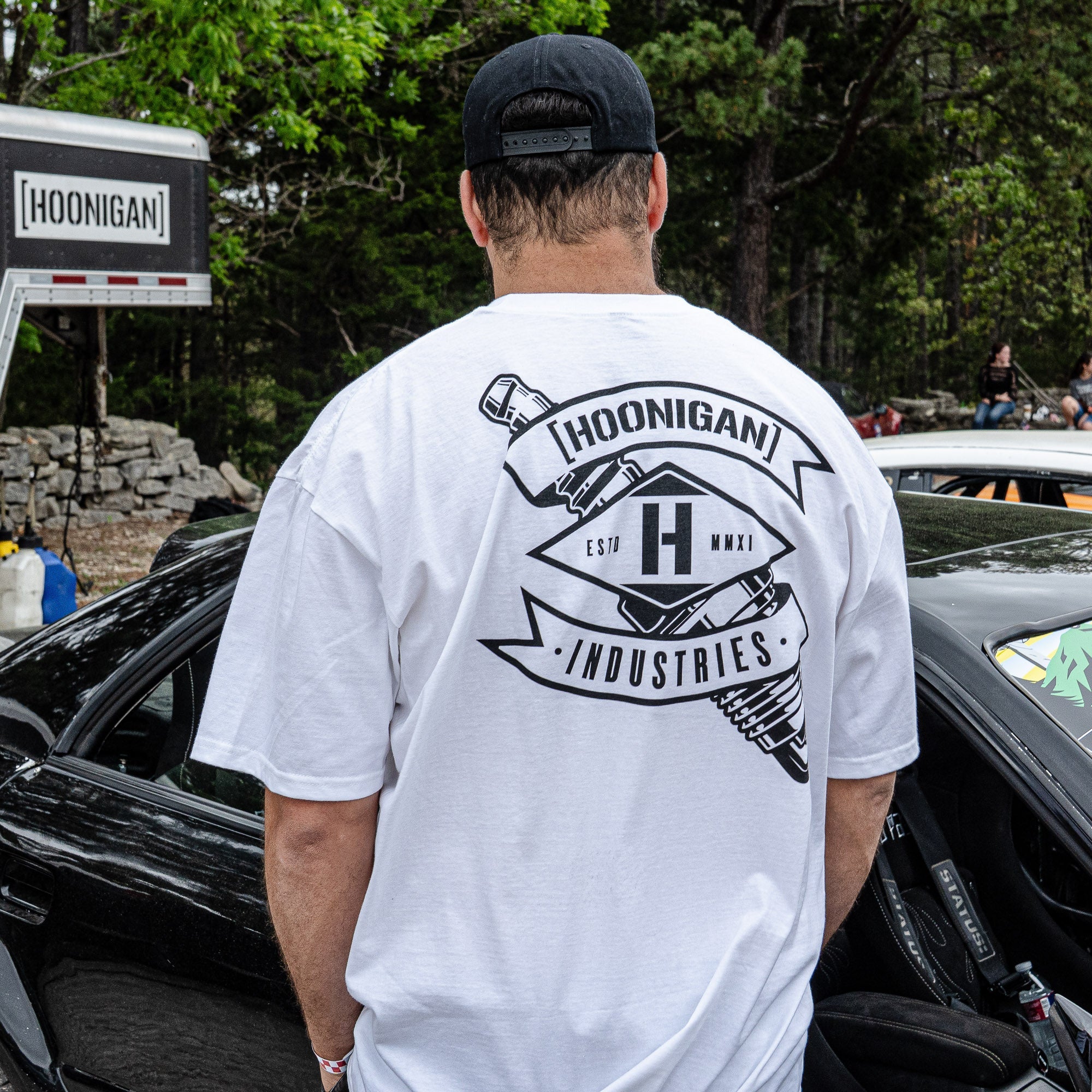 Man wearing a white Hoonigan LOW COMPRESSION short sleeve t-shirt, showcasing a bold graphic on the back.