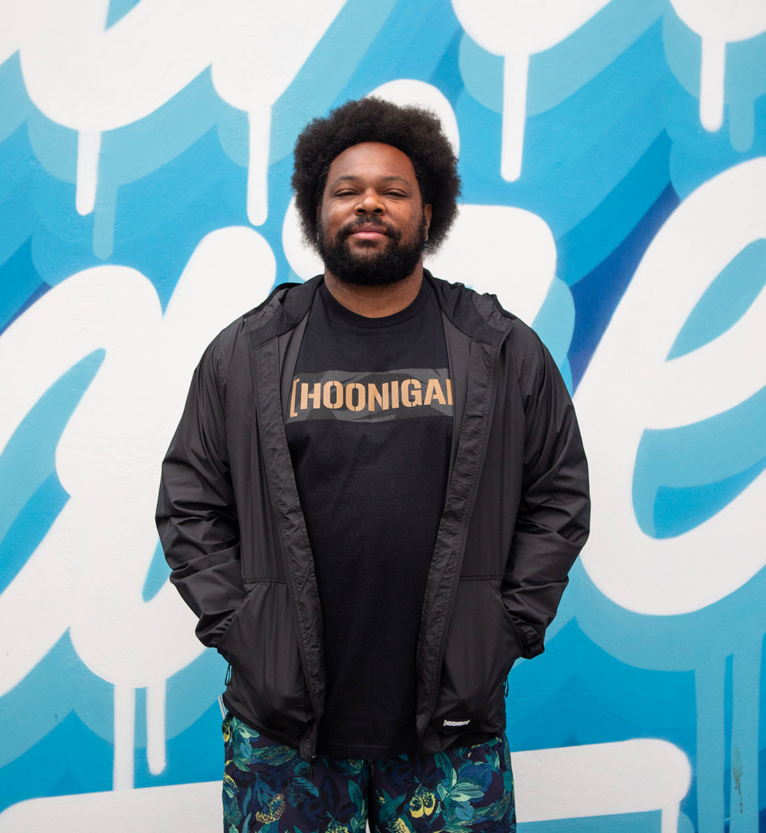 Hoonigan STANDARD ISSUE windbreaker jacket in black and white with logo detail, displayed against an outdoor backdrop.