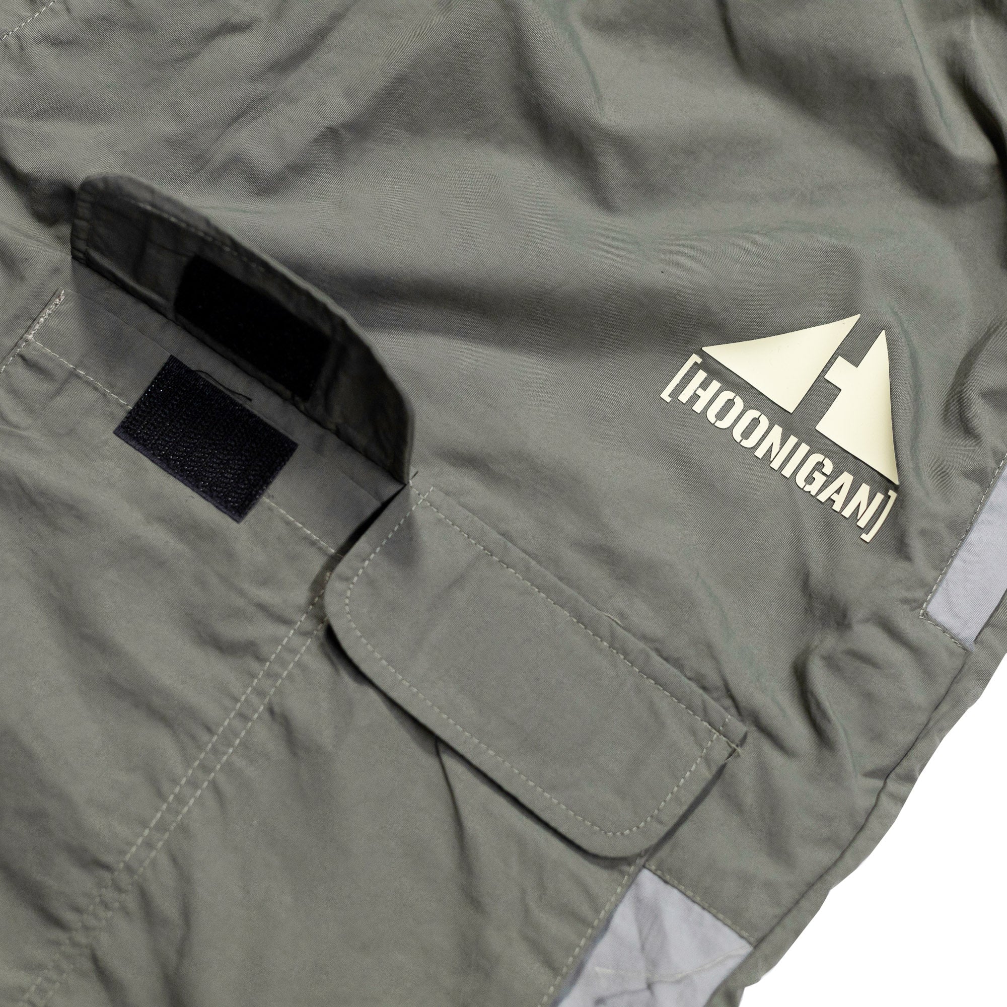 Close-up of gray Hoonigan H.A.V.O.C. rain-activated cargo shorts featuring a logo patch, Velcro pocket, and durable fabric.