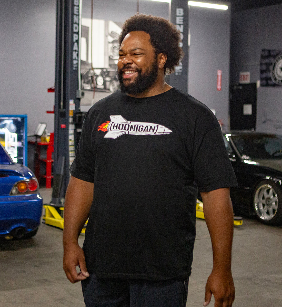 Hoonigan ROCKET Short Sleeve Tee featuring a vibrant graphic design on a black background, model wearing the shirt outdoors.