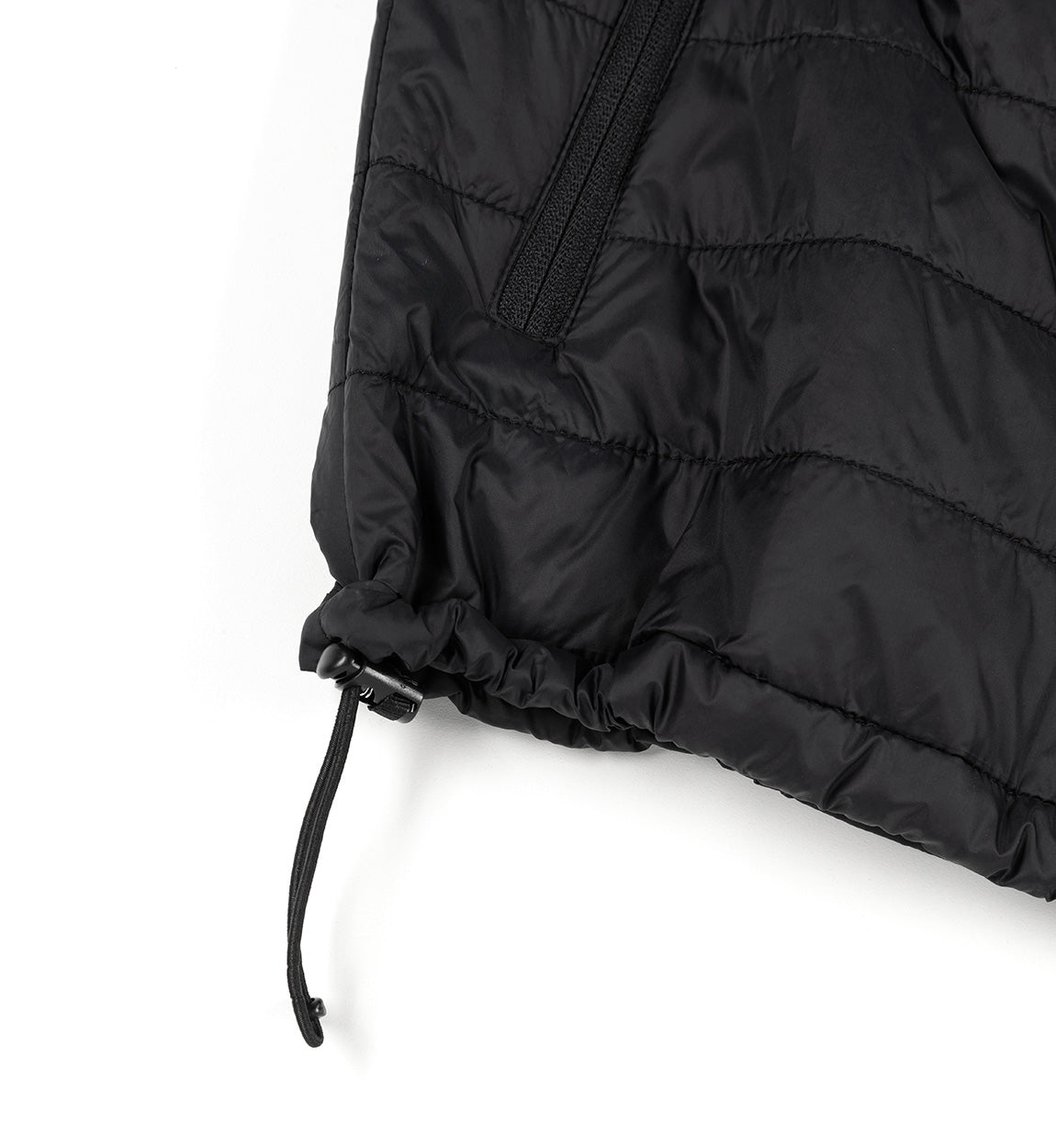 Close-up of a black GRILLE puffer vest showing quilted fabric, a zippered pocket, and an adjustable drawstring at the hem.