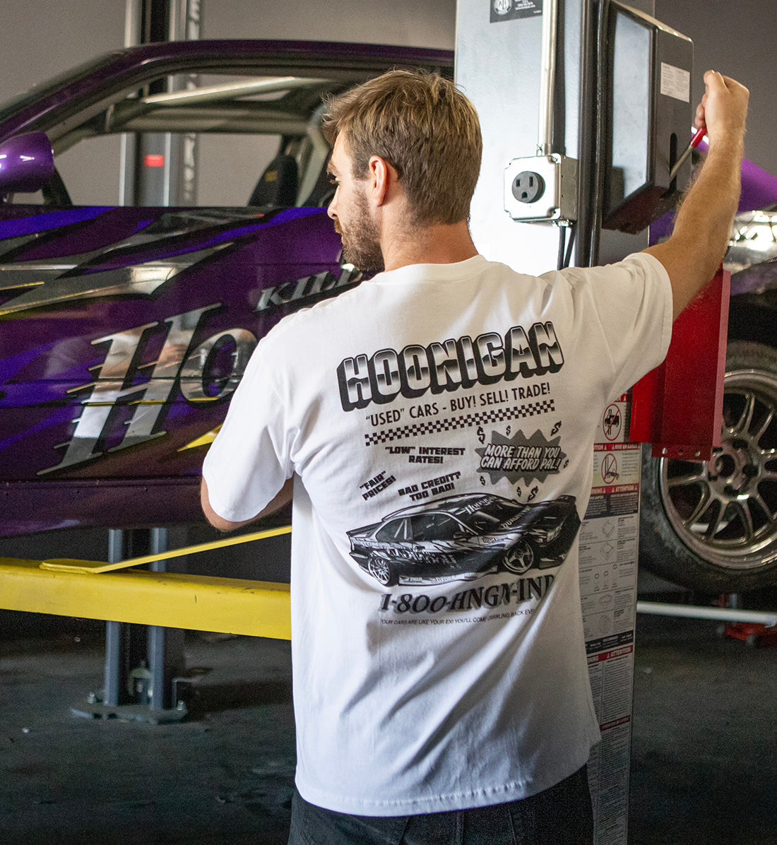 Hoonigan USED CARS Short Sleeve Tee in white, featuring a lifestyle image showing the back design.
