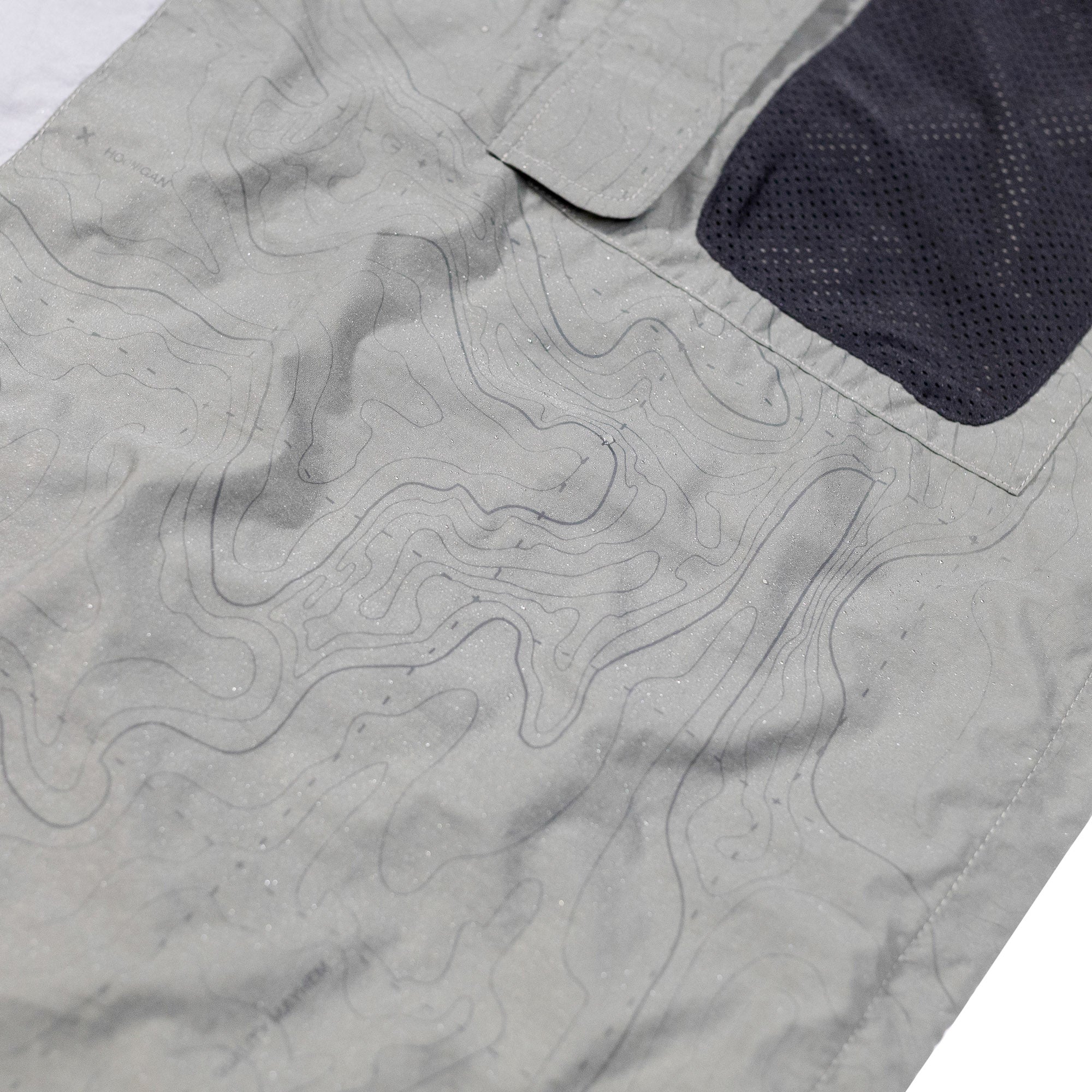 Close-up of the Hoonigan H.A.V.O.C. rain-activated windbreaker jacket showing water-sensitive fabric with topographical line design and a black mesh pocket.