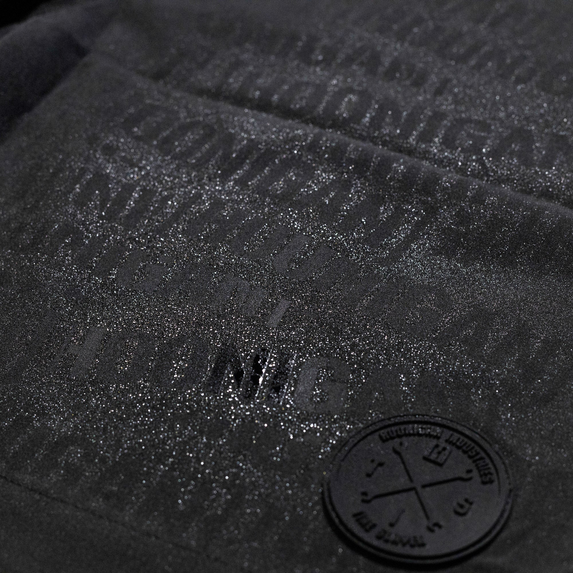 Close-up of Hoonigan Oil Slick Board Shorts featuring a textured logo and subtle sheen for a stylish, sporty look.