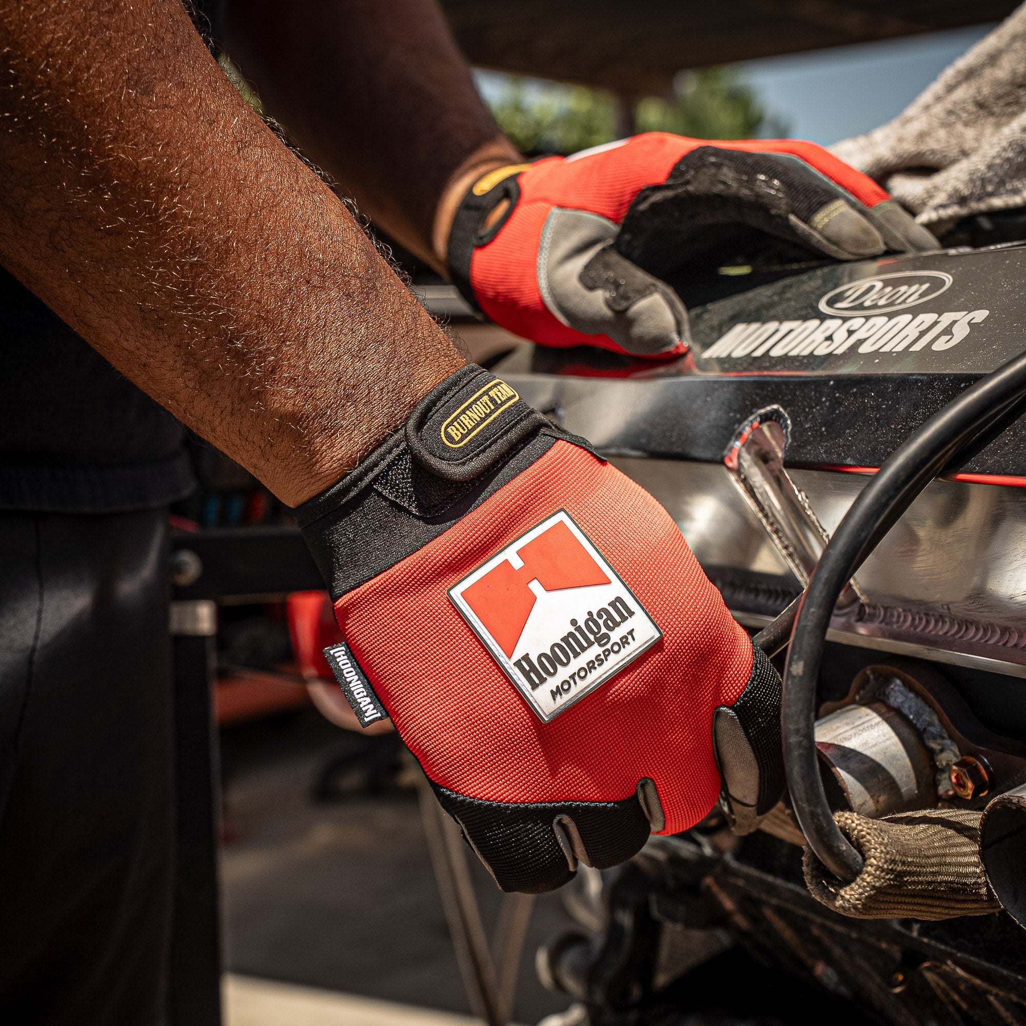 Hoonigan Surgeon General gloves worn by a mechanic working on a car engine, showcasing durability and style.