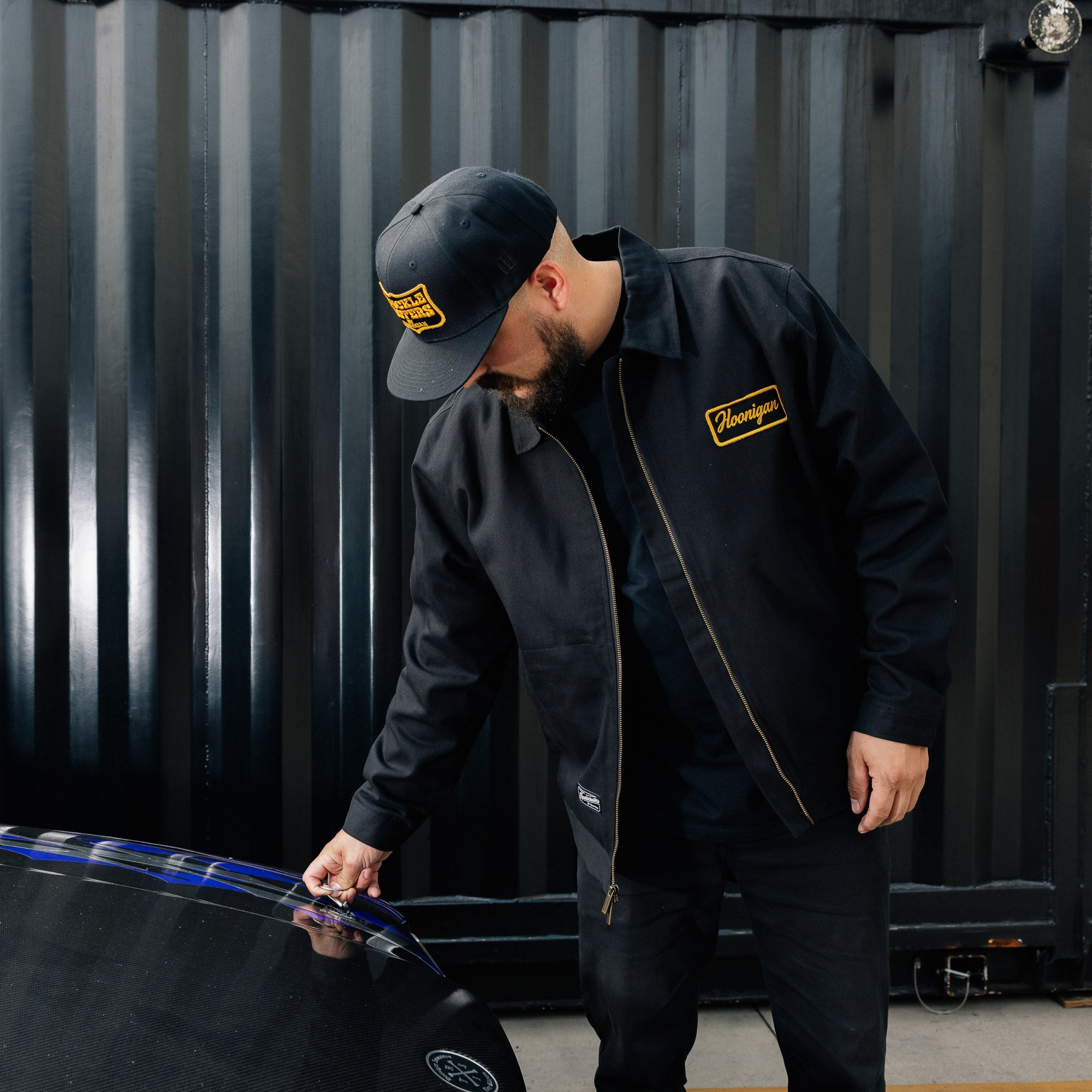 Hoonigan KNUCKLEBUSTERS jacket featuring a black classic design with the Hoonigan logo on the back and chest, ideal for motorsport enthusiasts.