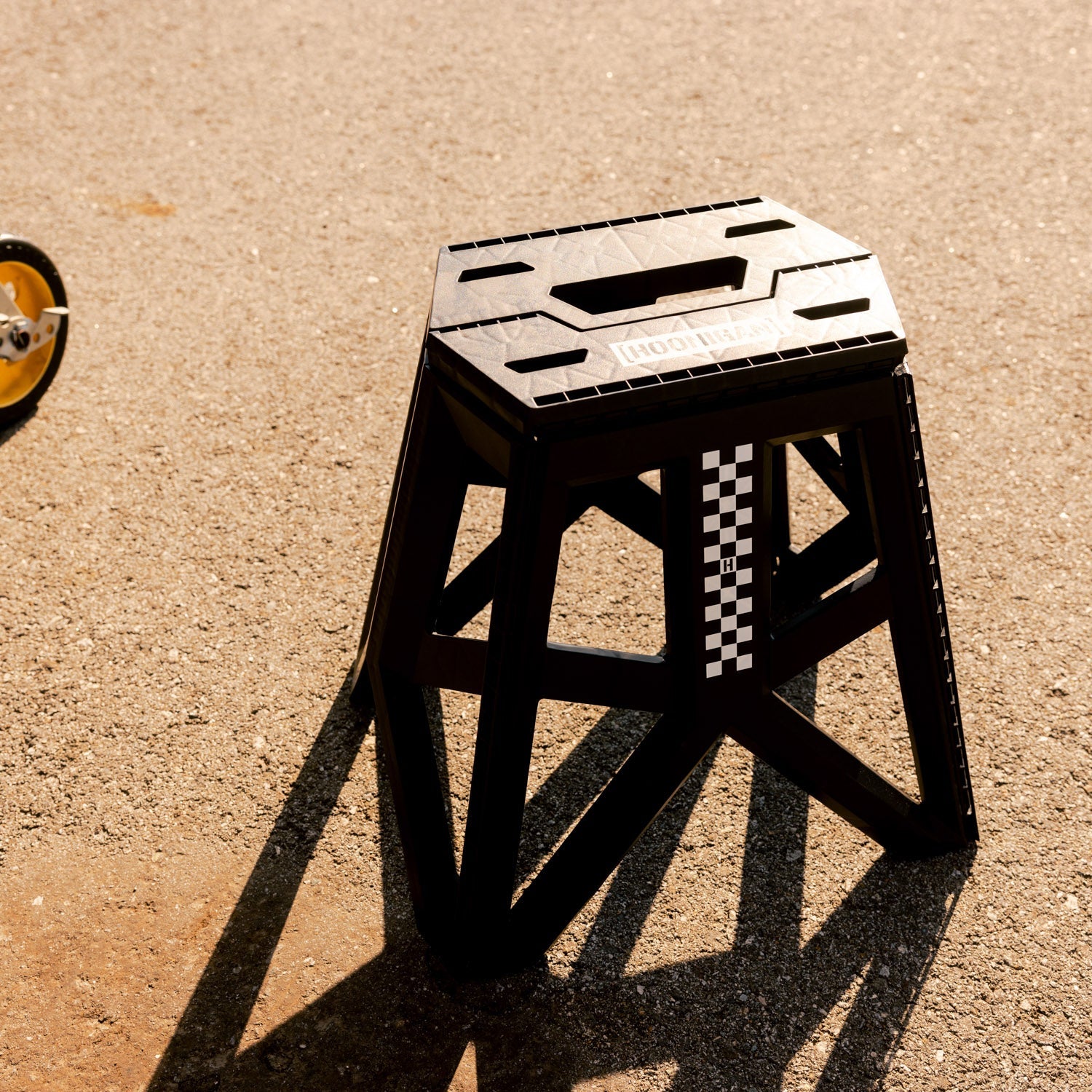 Hoonigan TRACK DAY collapsible stool with a logo, black fabric seat, and sturdy metal frame, designed for outdoor use.