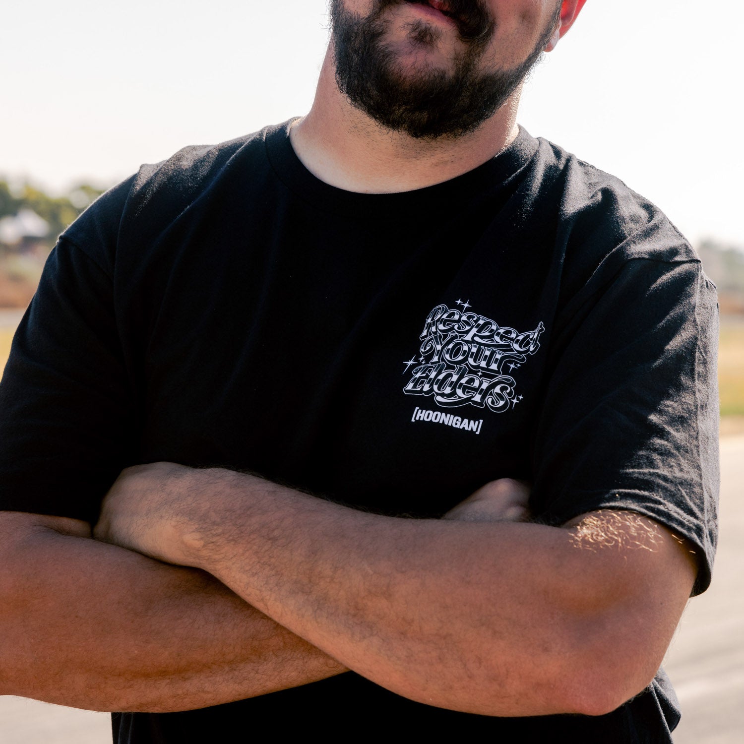 Black short sleeve tee featuring the phrase "RESPECT YOUR ELDERS" in bold white letters, overlaid with a Hoonigan logo. Ideal for motorsport enthusiasts.