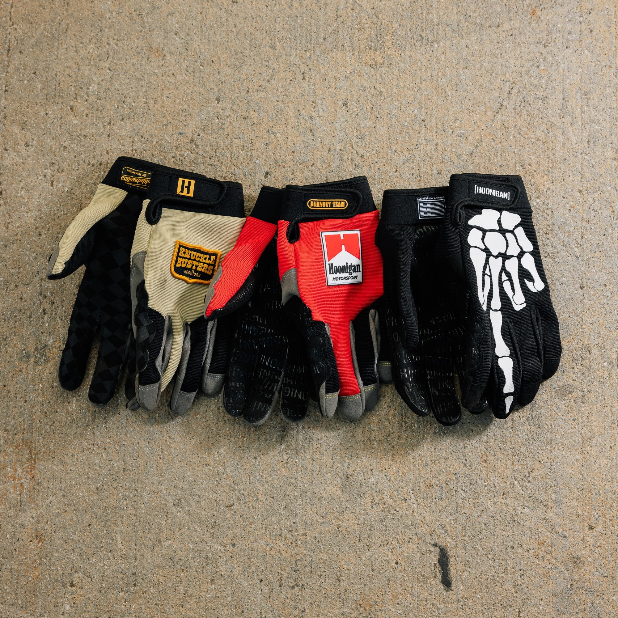 Hoonigan KNUCKLEBUSTERS gloves featuring a black design with bold white lettering and reinforced knuckles, ideal for motorsport enthusiasts.