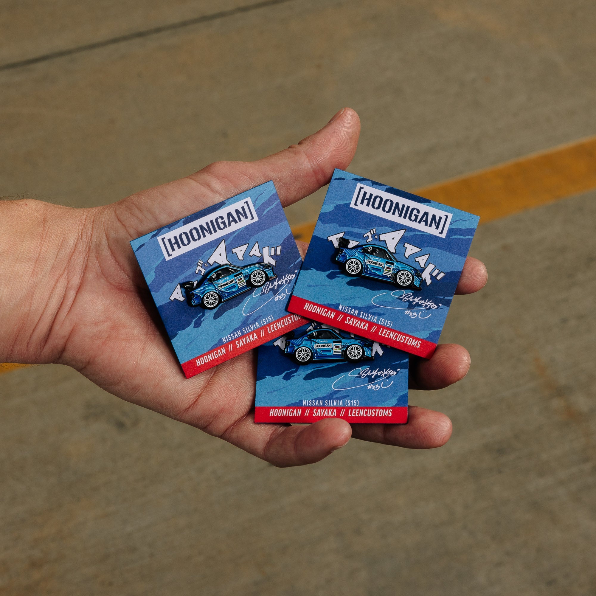 Hoonigan X Sayaka X Leen Customs Drifting Sayaka collectible pin featuring a detailed character design with vibrant colors on a sleek backing.