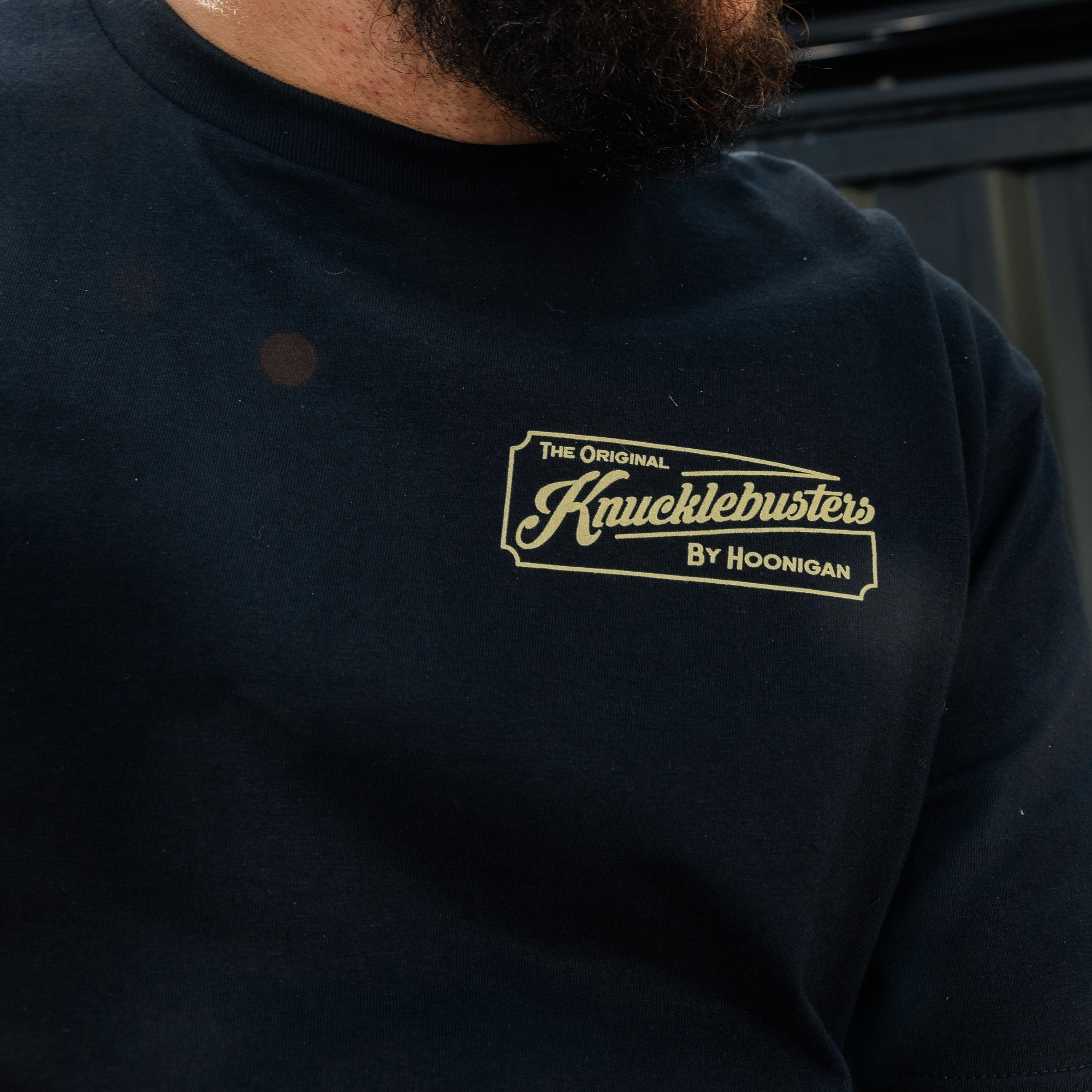 Black short sleeve tee featuring "Hoonigan Knucklebusters Auto Repair" graphic design on the front.