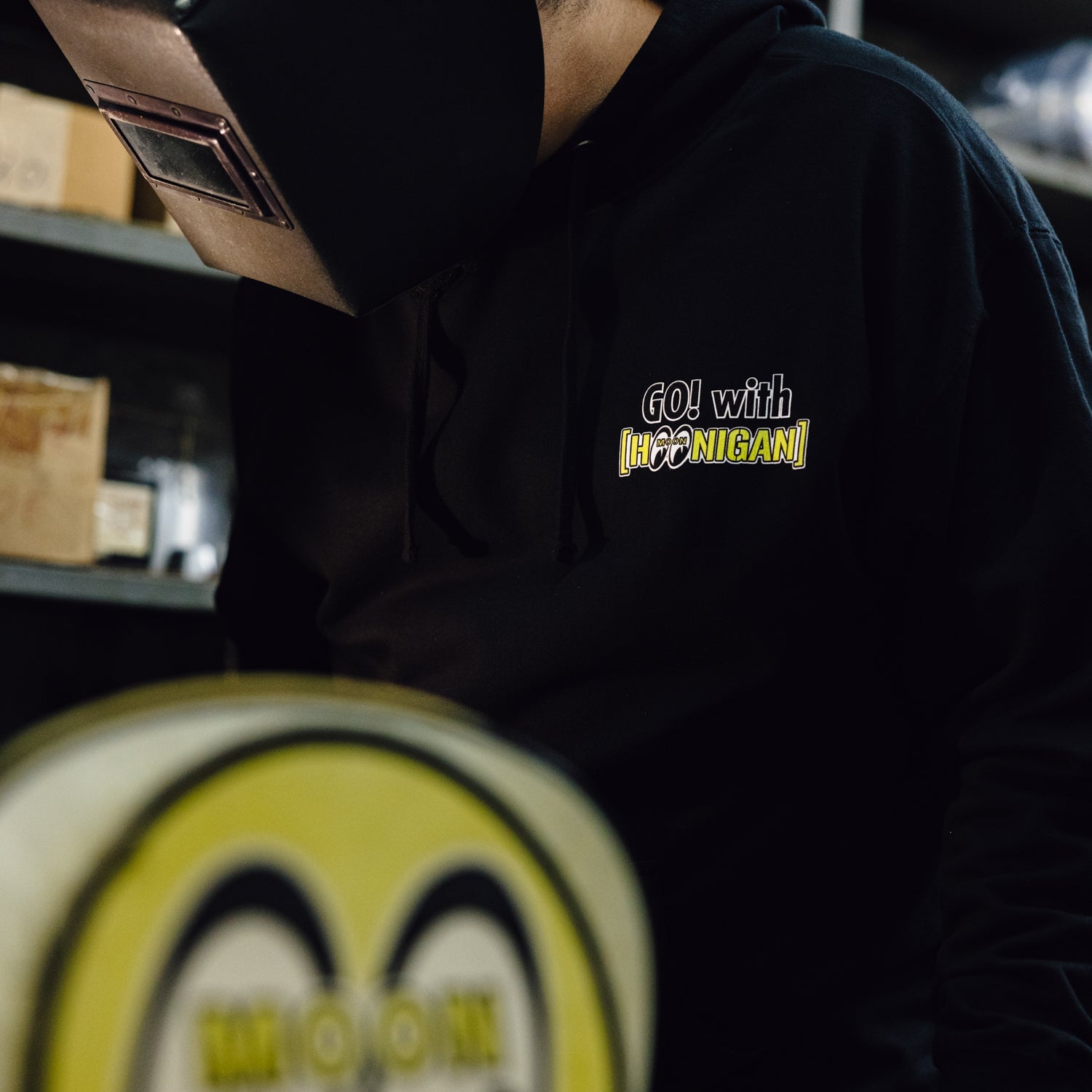 Black pullover hoodie featuring Hoonigan x Mooneyes branding, perfect for motorsport enthusiasts and car culture fans.