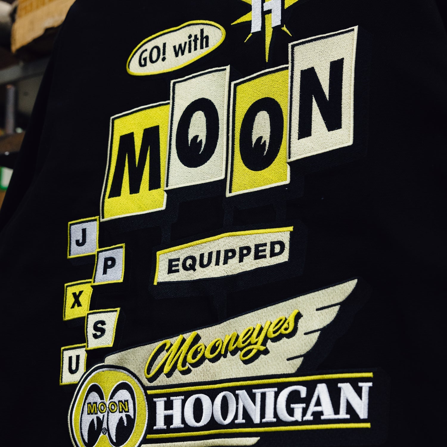 Hoonigan x Mooneyes MOON MOTEL Jacket featuring a black base with colorful graphics and logo details.