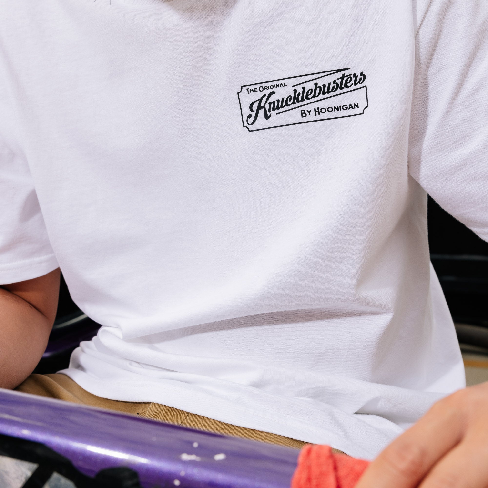 Black short sleeve tee featuring "Hoonigan KNUCKLEBUSTERS AUTO REPAIR" graphic on the front.