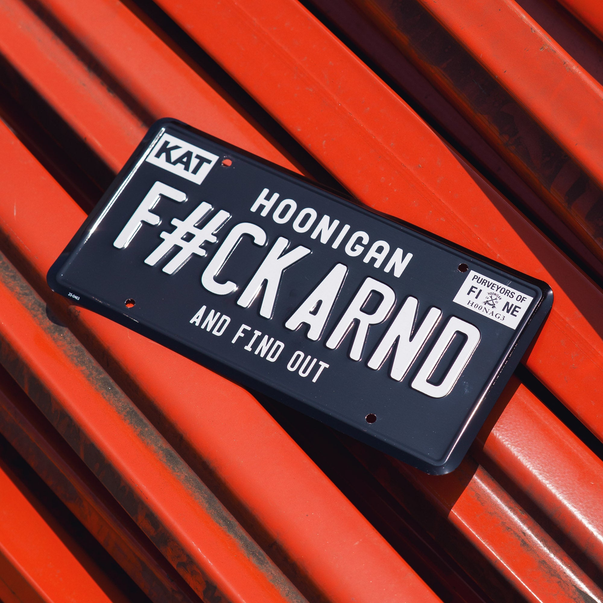 Black license plate with white text reading "FCK ARND" and "and find out," featuring a "Hoonigan" logo and a small sticker in the corner.