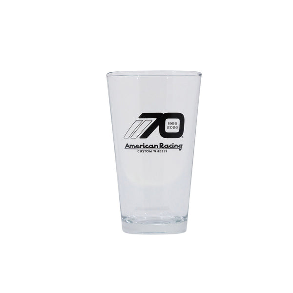 Clear pint glass featuring the American Racing logo and a 70th anniversary design, ideal for motorsport enthusiasts.