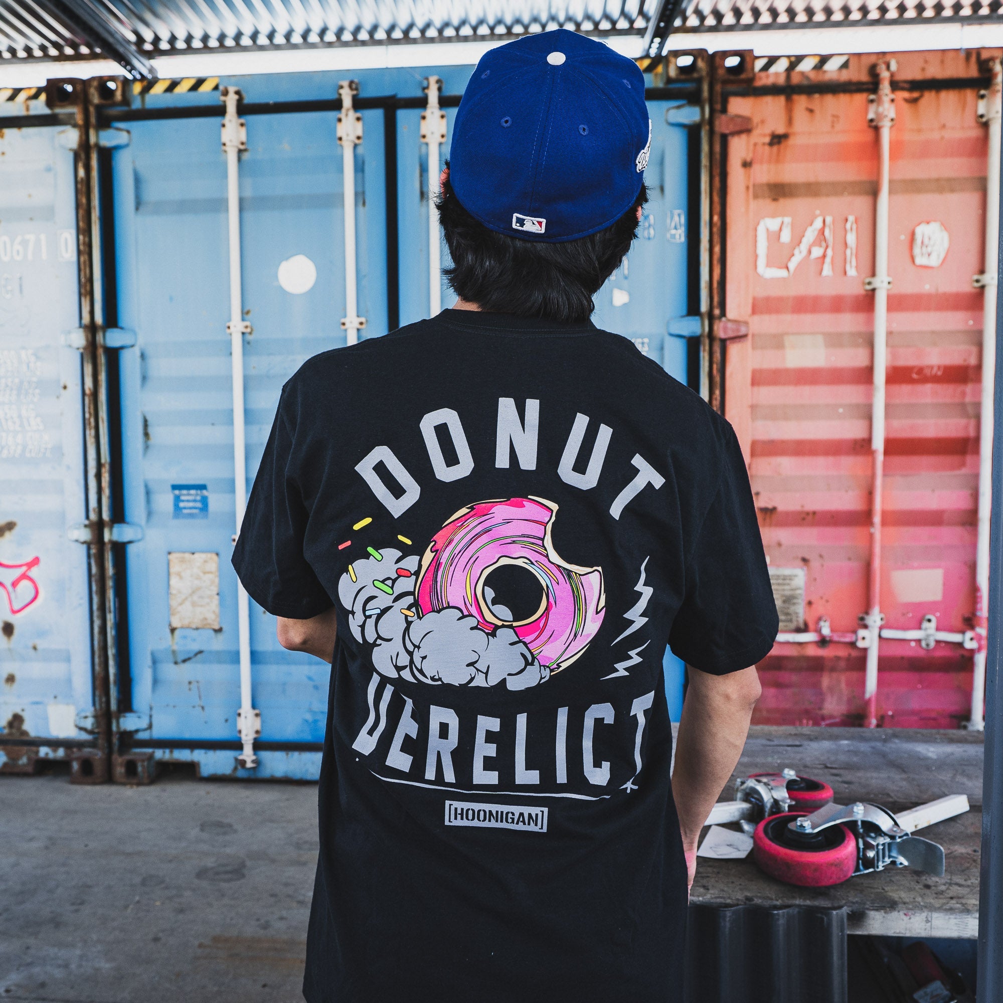Black short sleeve Hoonigan t-shirt featuring a colorful donut graphic with "DONUT DERELICT" text on the back.
