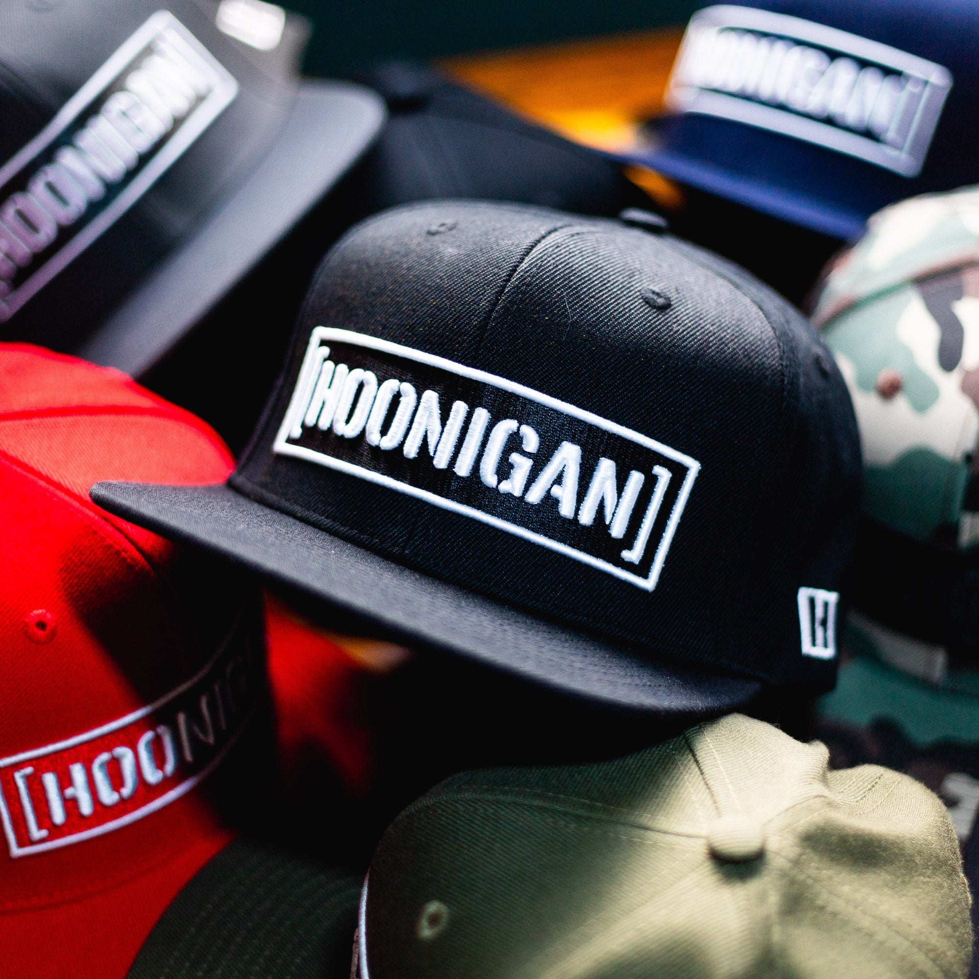 Hoonigan CENSOR BAR Snapback Hat in black surrounded by various colors and styles, showcasing automotive lifestyle apparel.