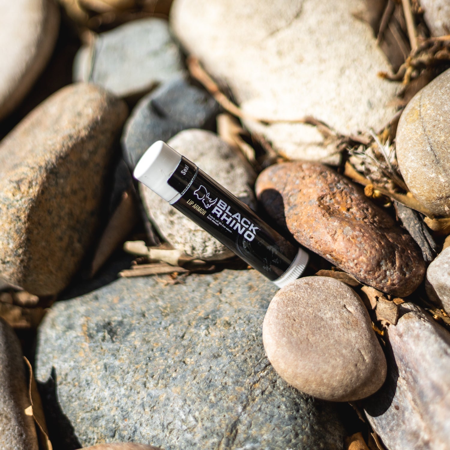 Black Rhino LIP ARMOR lip balm tube, featuring a sleek black design with bold branding, positioned on a wooden surface.