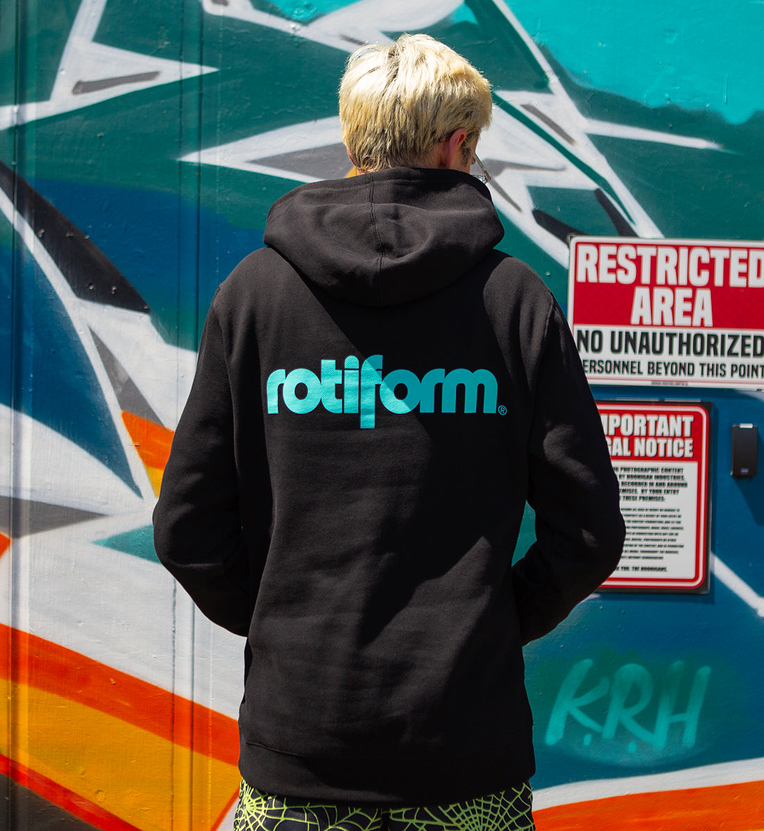 Black and teal Rotiform STAPLE hoodie with logo, shown from the back in a lifestyle setting.