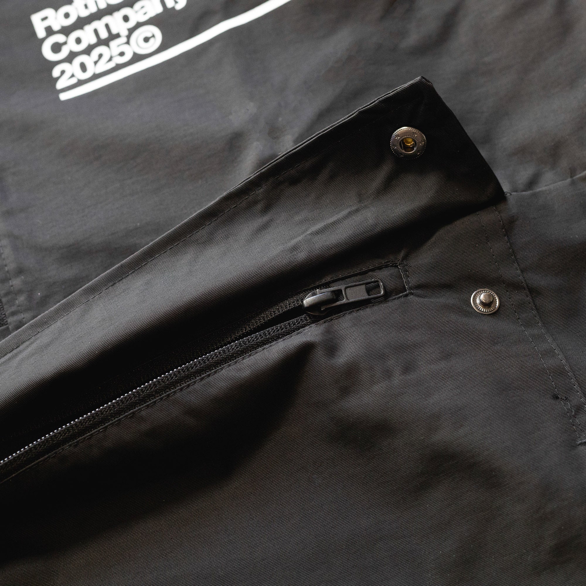 Close-up of the black Rotiform GLOBAL IMPACT Half Zip Anorak Jacket showing a zipper, snap buttons, and fabric details.