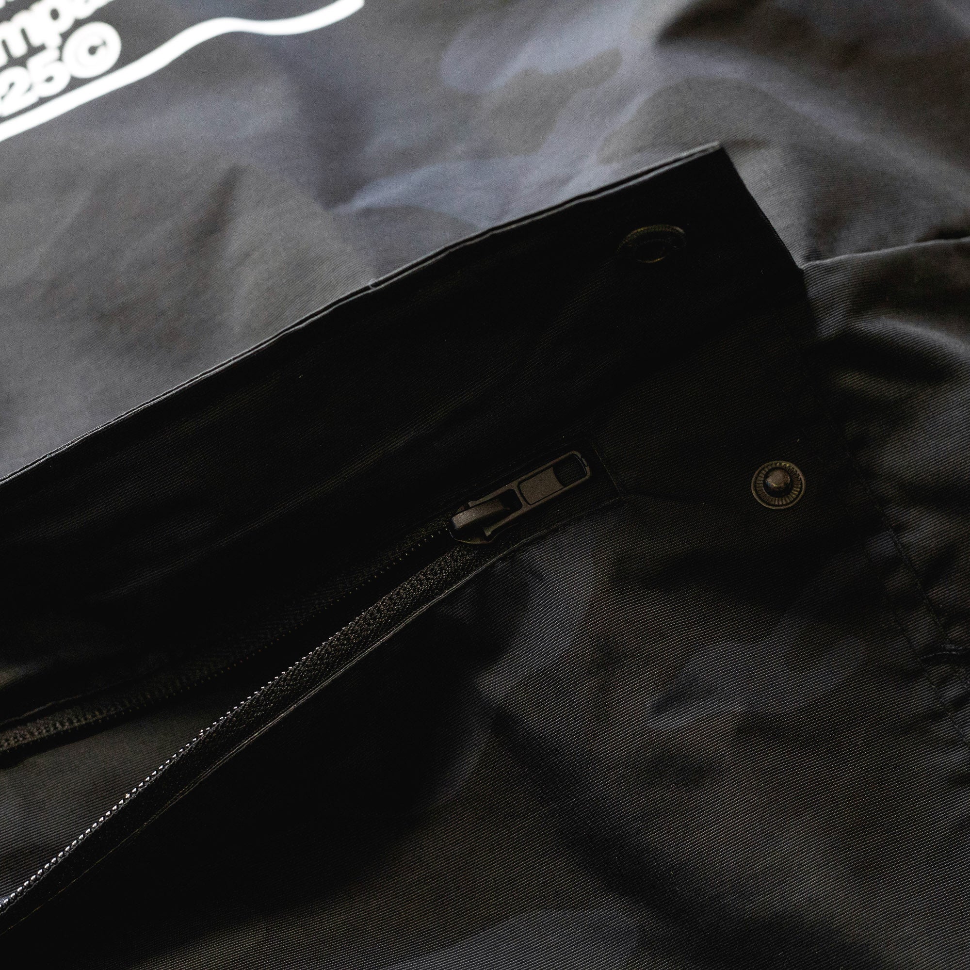 Close-up of the black Rotiform GLOBAL IMPACT half zip anorak jacket showing a zippered pocket and snap button details.