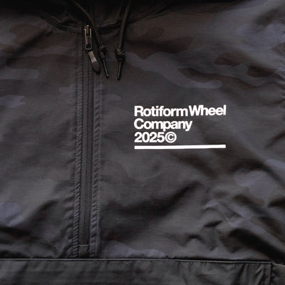 Close-up of a black Rotiform GLOBAL IMPACT Half Zip Anorak Jacket with white text, zipper, and drawstrings on the collar.