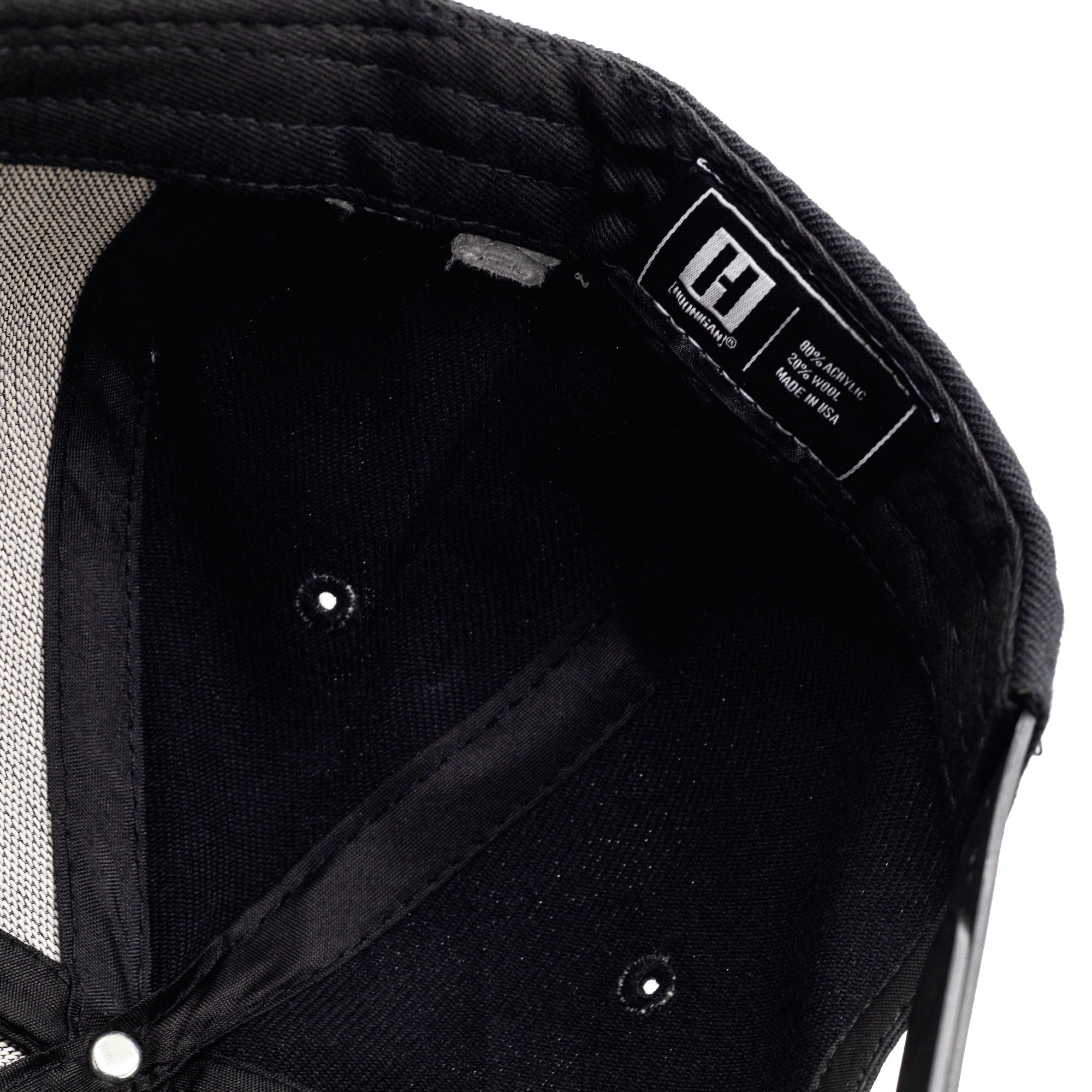 Inside view of a black Hoonigan KB43VER 43i snapback hat with a label indicating 100% acrylic, 20% wool, made in the USA.
