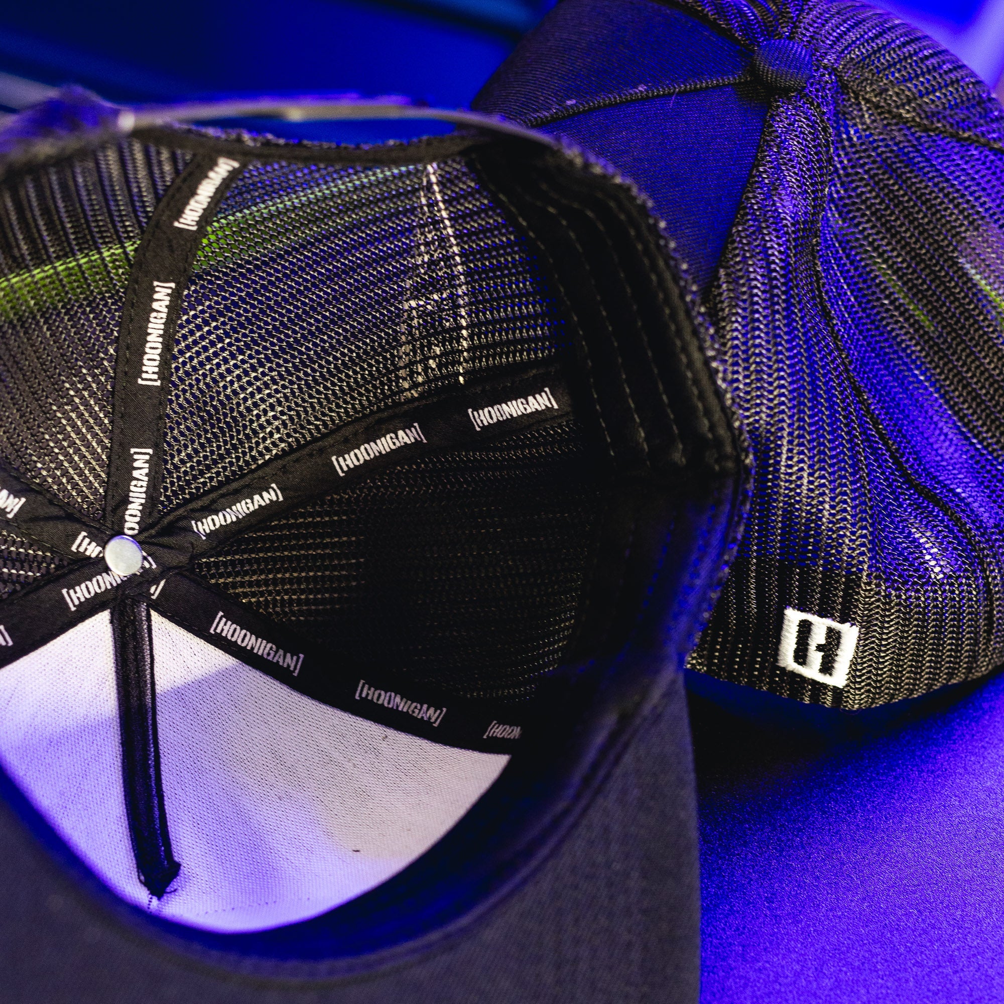 Close-up of a black Hoonigan HITS V2 trucker hat showing interior mesh lining, branded tape, and a partial view of the hat's structured crown.
