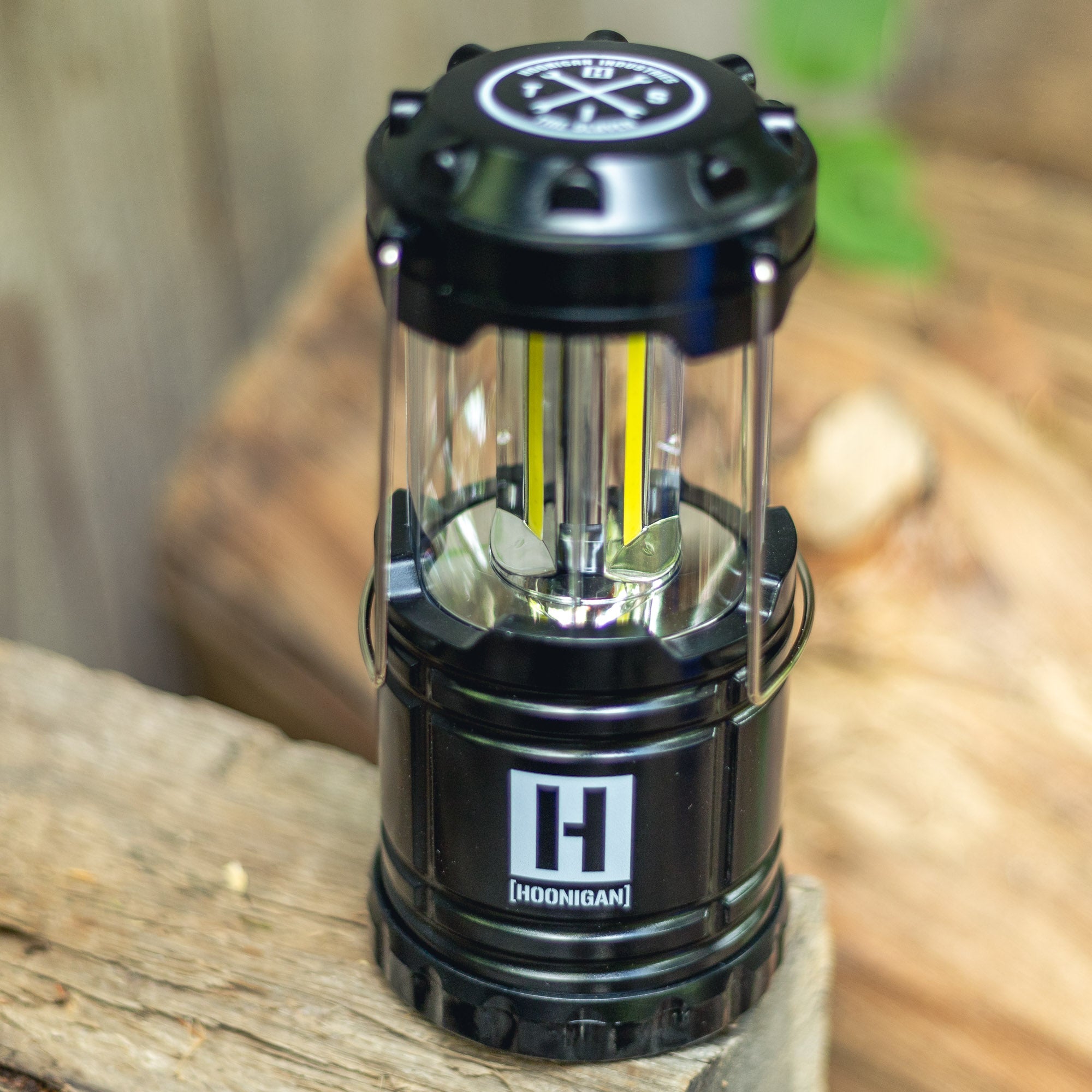 Hoonigan H.A.V.O.C. lantern with black body, clear protective casing, and LED light strips, placed on a wooden surface outdoors.