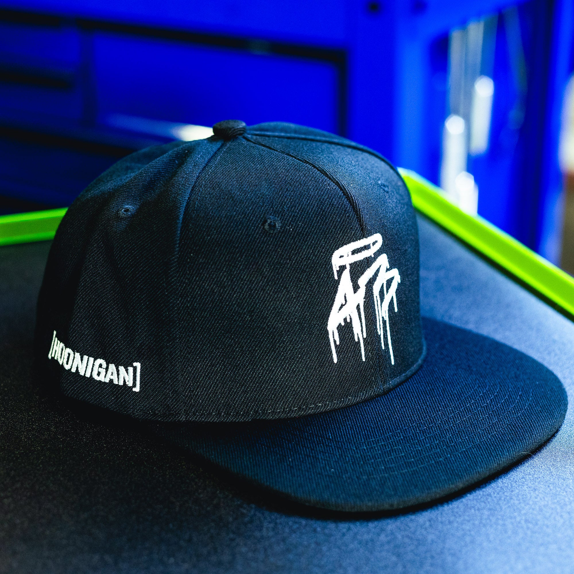 Black snapback hat with white "HOONIGAN" text and graphic design, featuring a curved brim and adjustable strap.