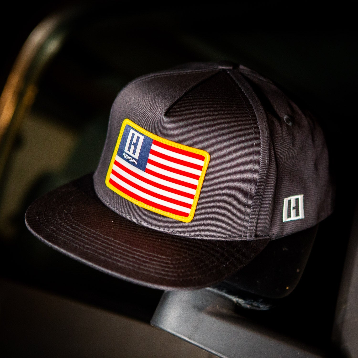 Hoonigan PATRIOT Snapback Hat featuring an American flag patch on a black cap, perfect for motorsport enthusiasts.