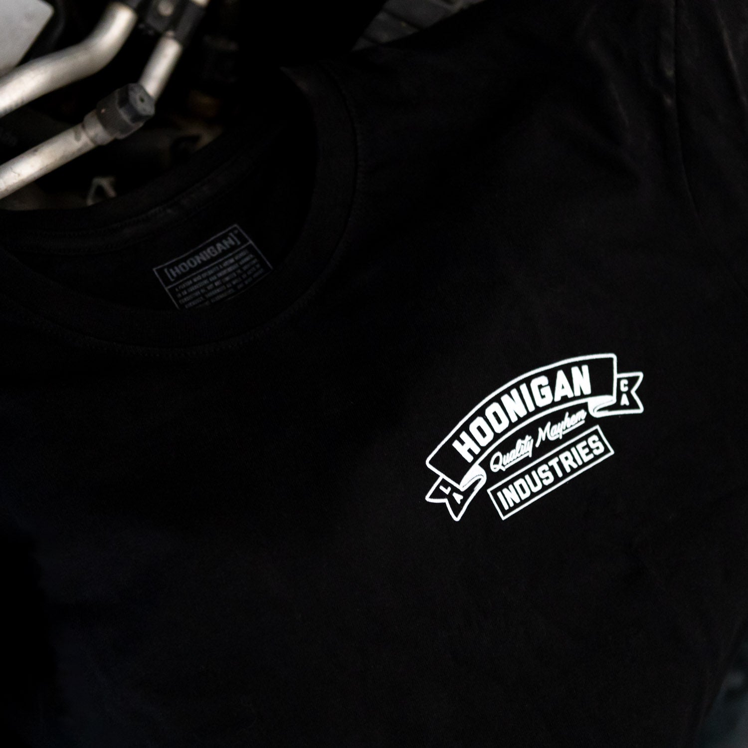 Black Hoonigan CRANKED short sleeve t-shirt featuring a bold white logo on the chest, laid on an engine.
