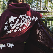Model wearing a maroon Hoonigan x Lia Block UR STAR pullover hoodie with a star graphic, leaning against a car.
