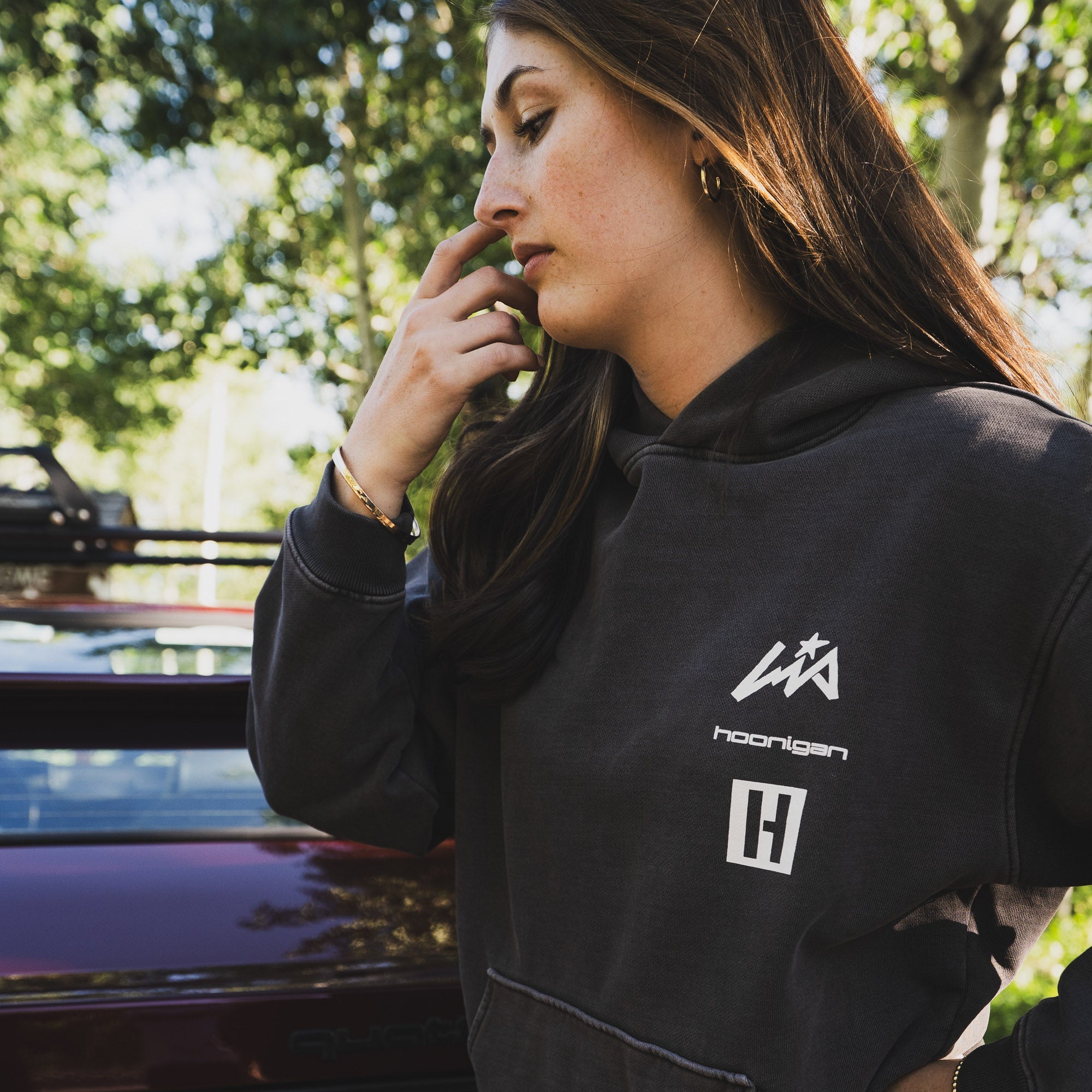 Woman wearing a Hoonigan x Lia Block vintage pullover hoodie, standing near a car in a sunny outdoor setting.