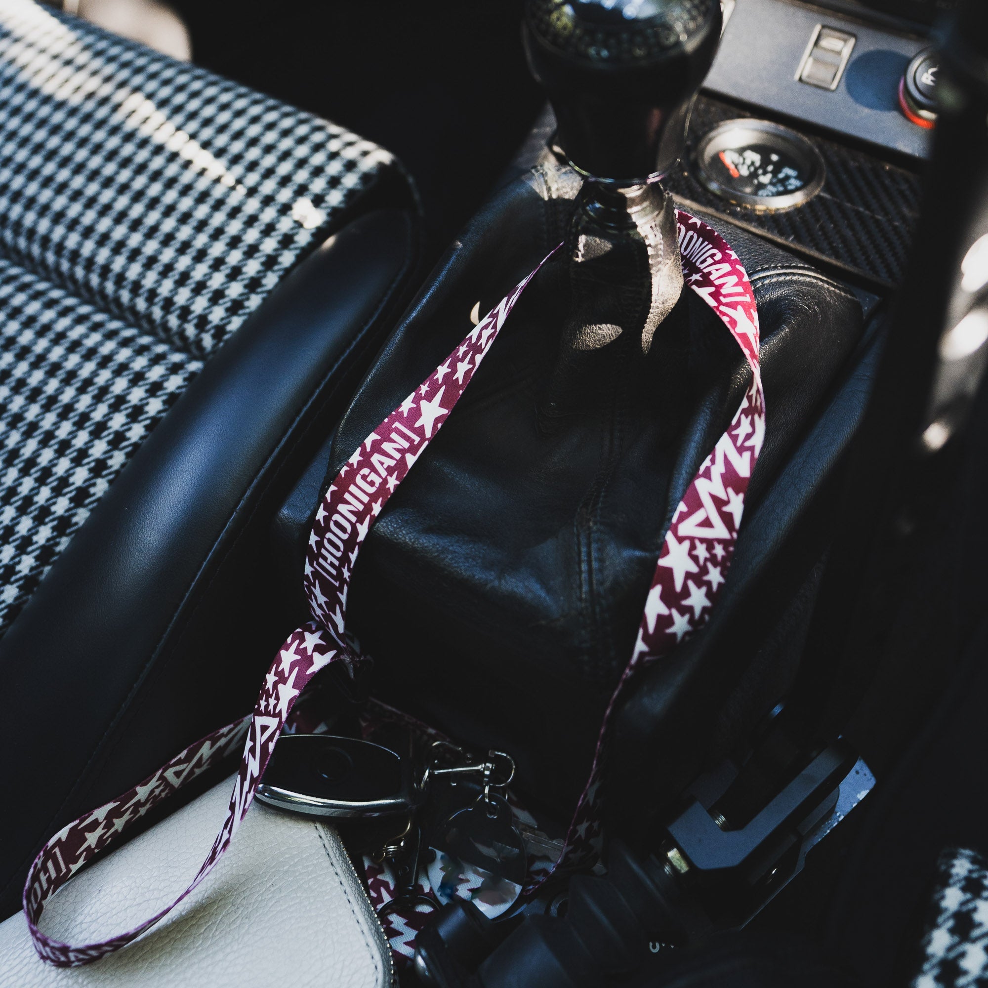 Hoonigan x Lia Block UR STAR lanyard resting on a car's gear shift, showcasing a bold design and automotive style.