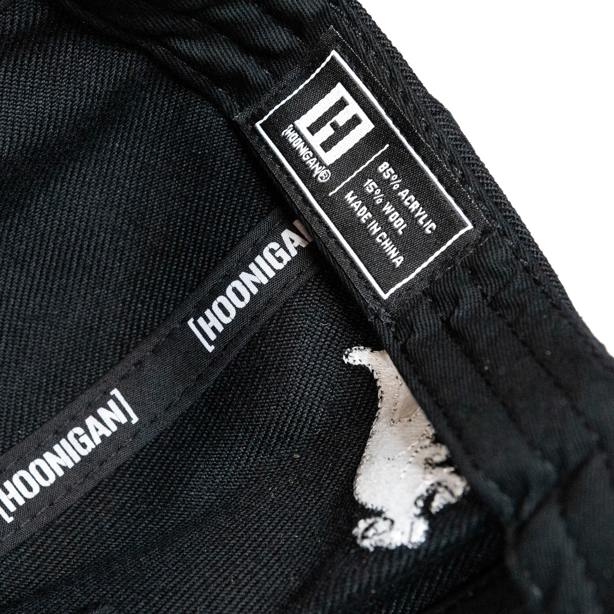 Interior tag of Hoonigan GYMKHANA AUSSIE SHRED SUBARU snapback hat showing fabric composition and brand logo.