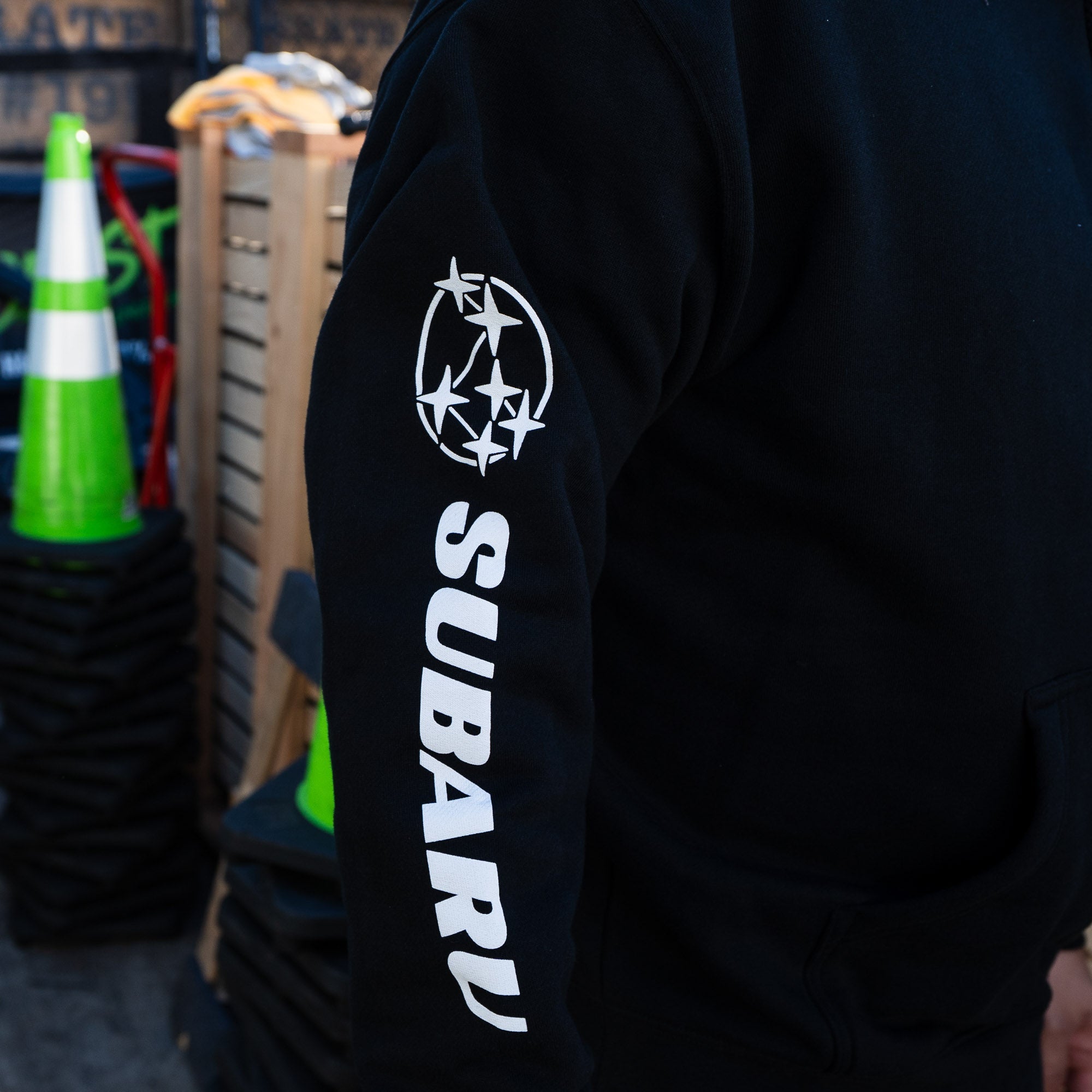 Black pullover hoodie featuring the Subaru logo and "SUBARU" text on the sleeve, ideal for motorsport enthusiasts.