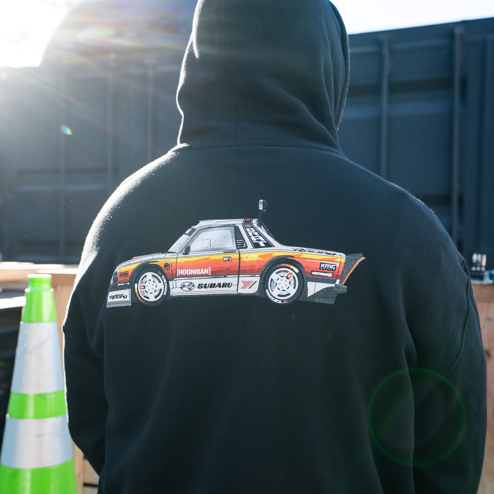 Black pullover hoodie featuring a colorful graphic of a Subaru car on the back, designed for motorsport enthusiasts.