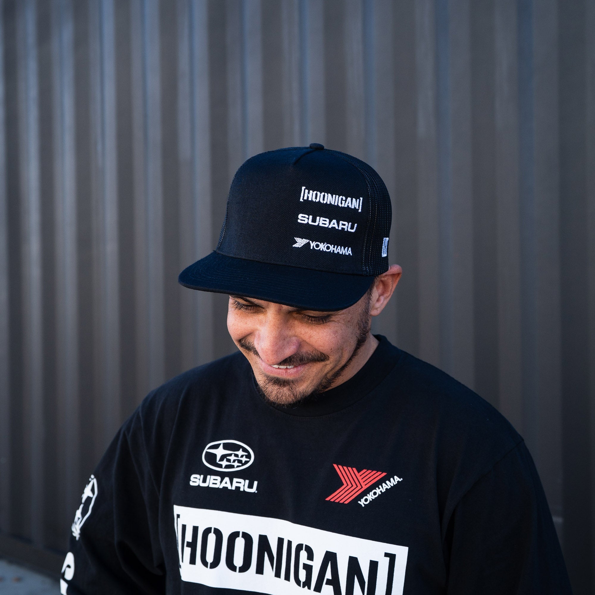 Hoonigan GYMKHANA AUSSIE SHRED ROLL CALL trucker hat worn by a man, featuring Subaru and Yokohama logos.