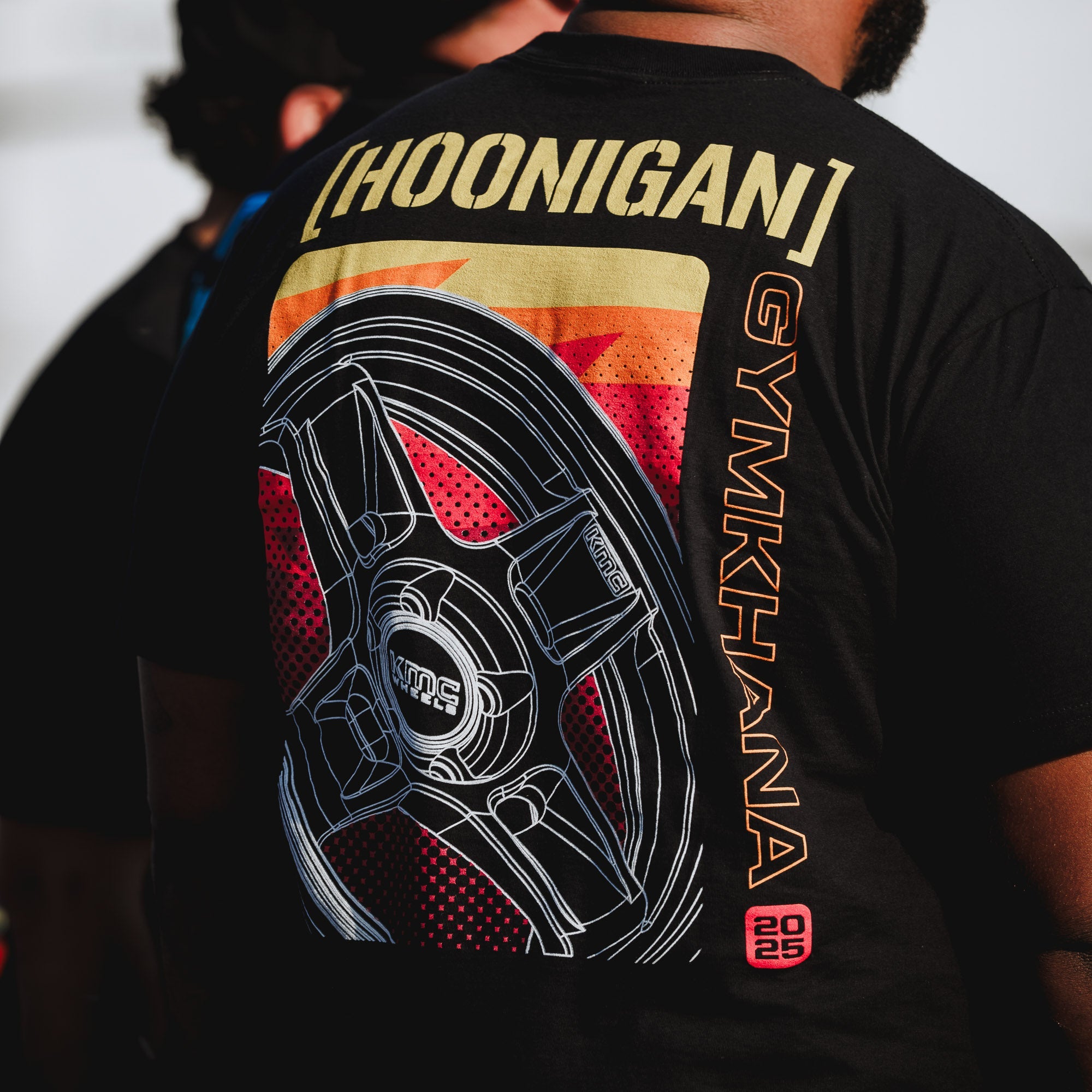 Black short sleeve t-shirt featuring a colorful graphic of a wheel and the text "Hoonigan GYMKHANA" on the back.
