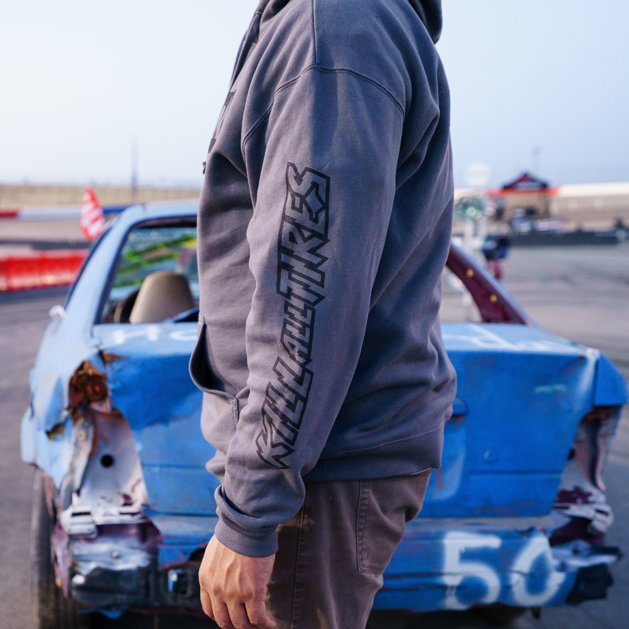 Hoonigan CENSOR BAR KILL ALL TIRES pullover hoodie worn by a person next to a damaged car, showcasing automotive culture.
