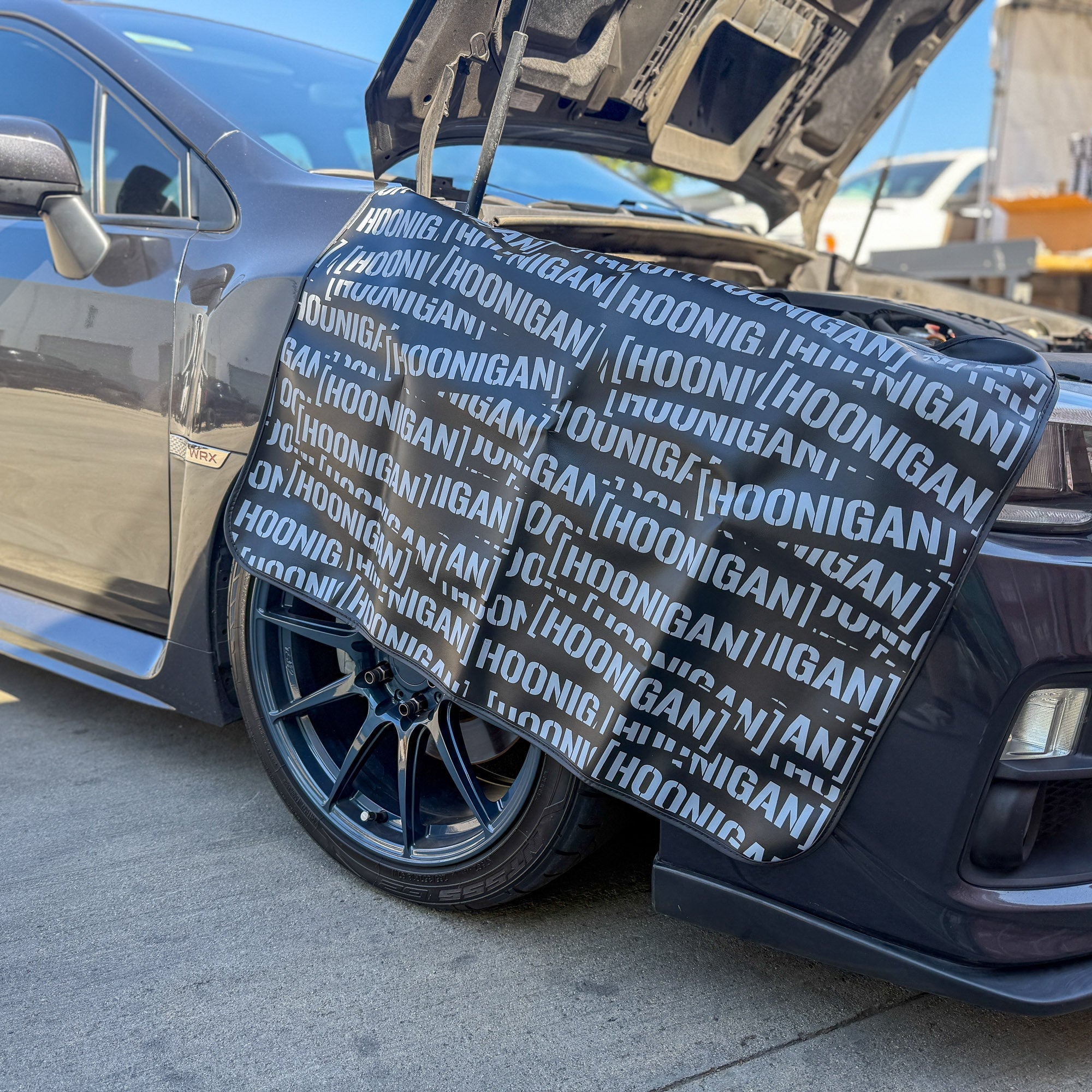 Hoonigan SCATTER PRINT Fender Cover displayed on a car, protecting the fender with a bold logo design.