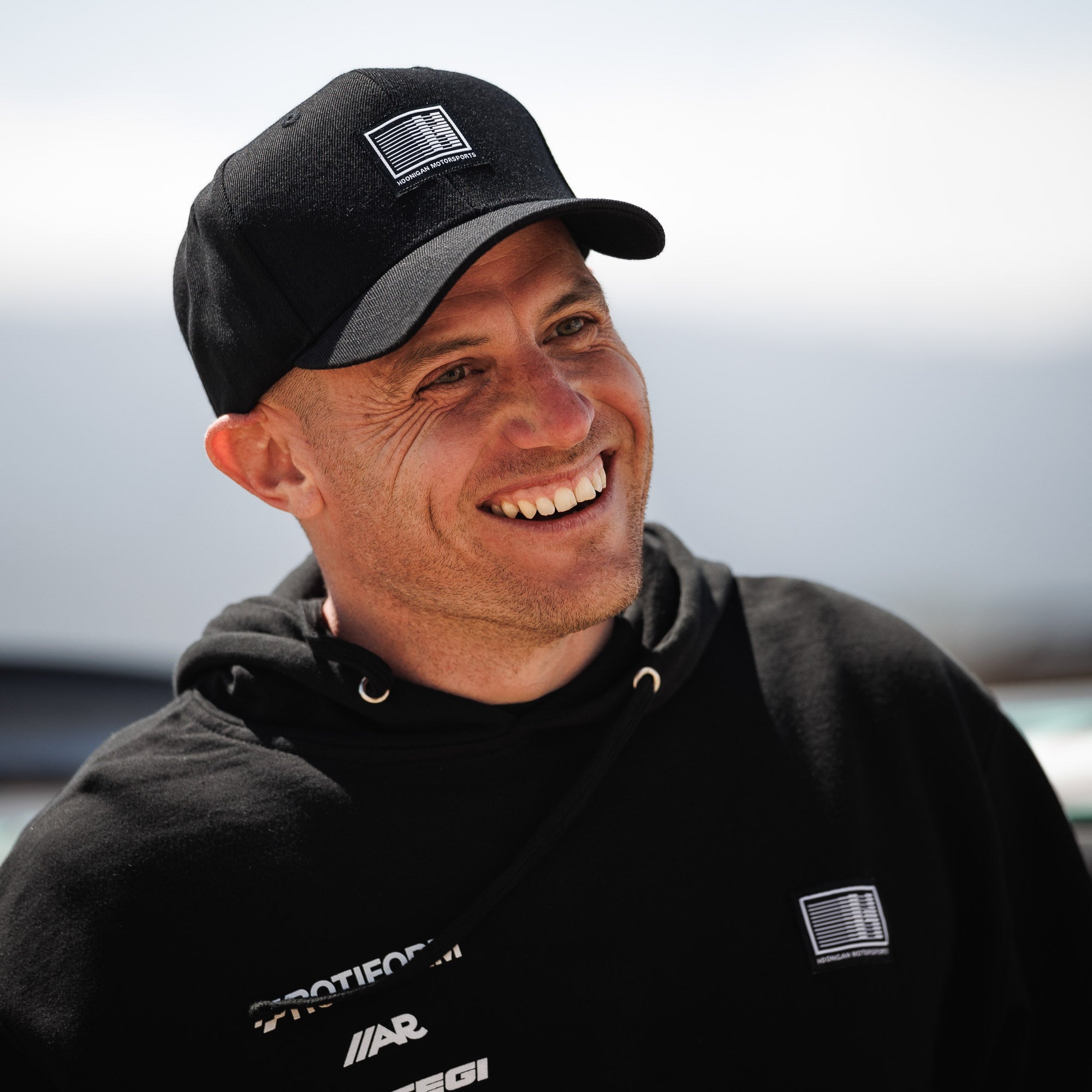 Hoonigan Motorsports snapback hat with black fabric and adjustable back strap, featuring a white logo on the front.