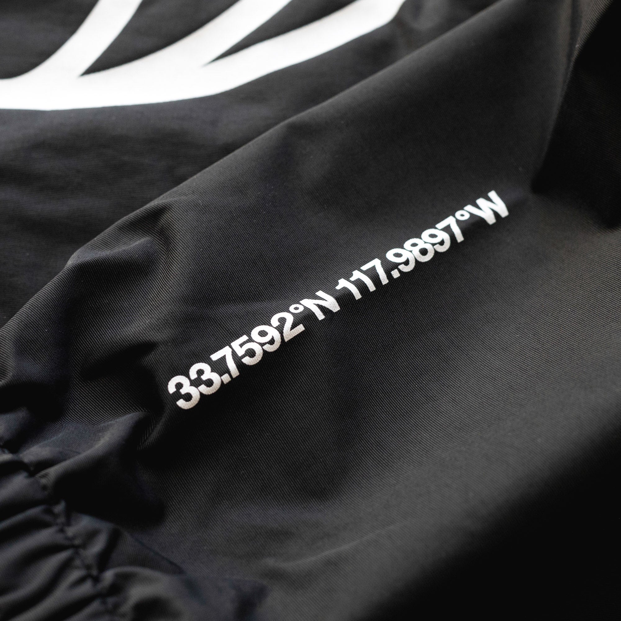 Close-up of a black Rotiform GLOBAL IMPACT half-zip anorak jacket with white coordinates printed on the fabric.