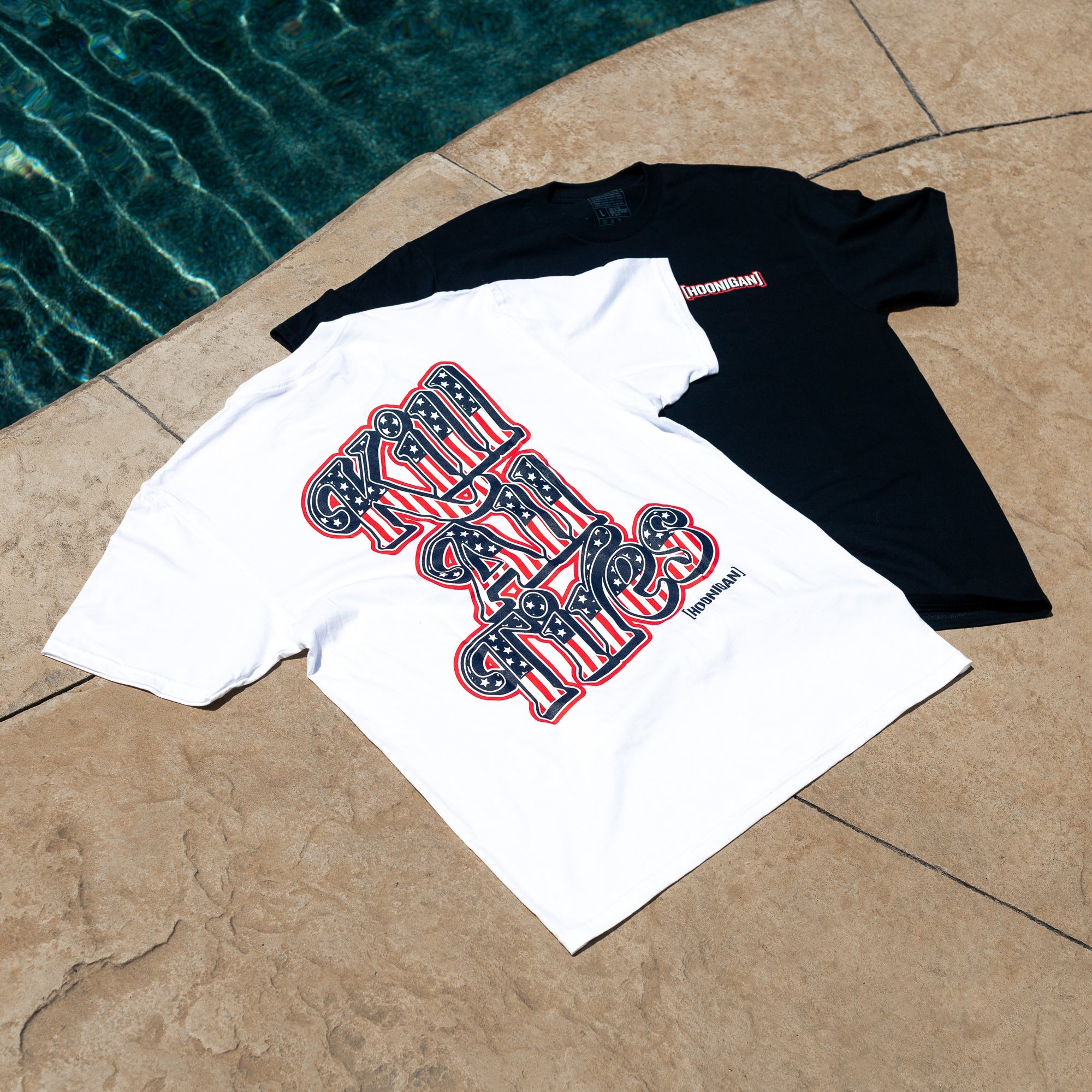 Two Hoonigan KILL ALL TIRES USA short sleeve T-shirts, one black and one white, laid on a poolside surface.