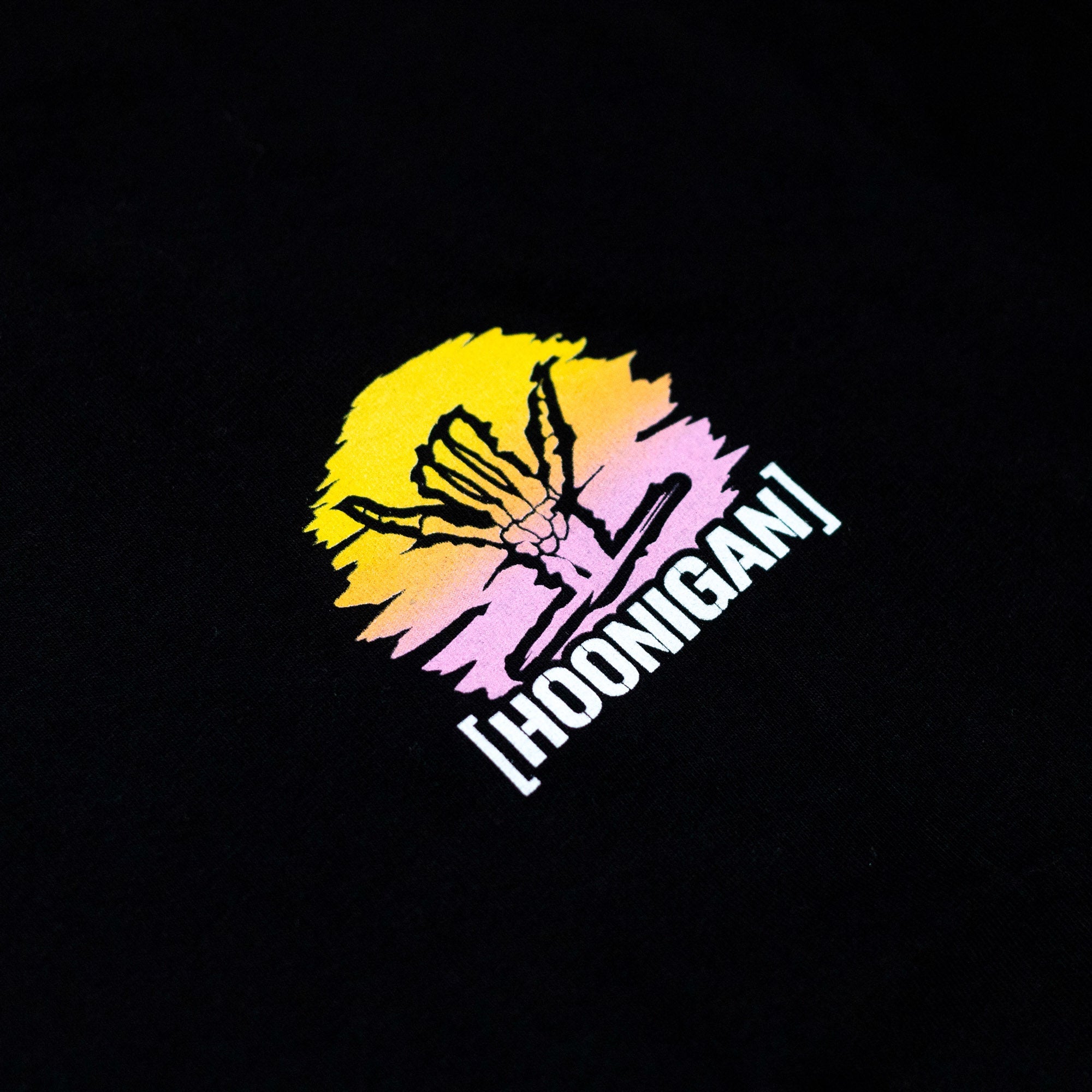 Black short sleeve t-shirt featuring a colorful Hoonigan x Shreddy graphic of a hand and sunset design.
