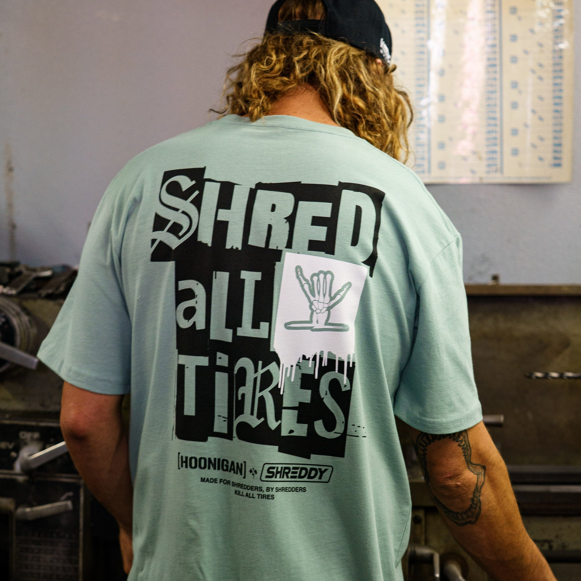 Men's mint green short sleeve t-shirt featuring bold "SHRED ALL TIRES" graphic on the back, perfect for motorsport enthusiasts.